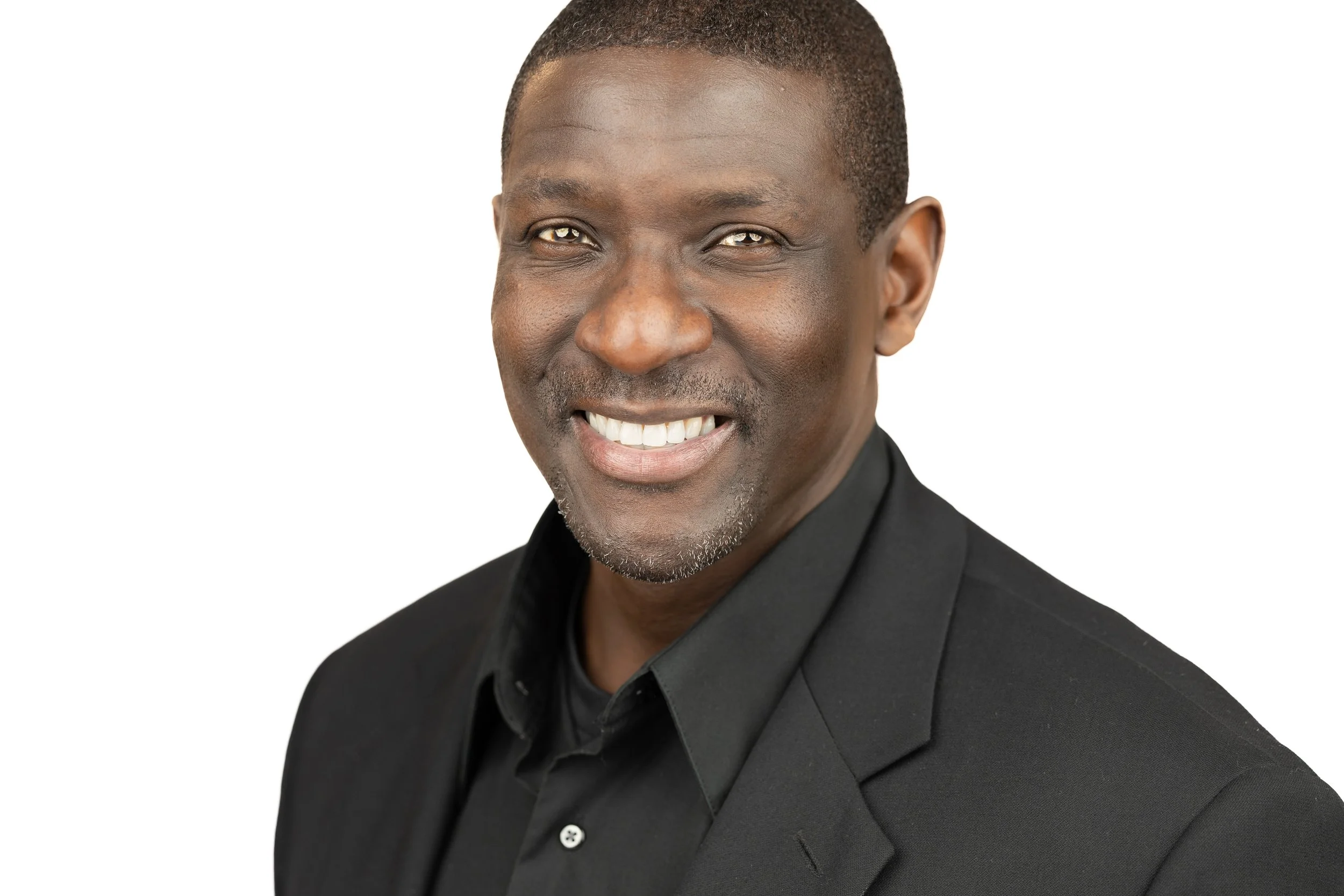 Headshot of a smiling African American man in a black suit and shirt, against a white background.