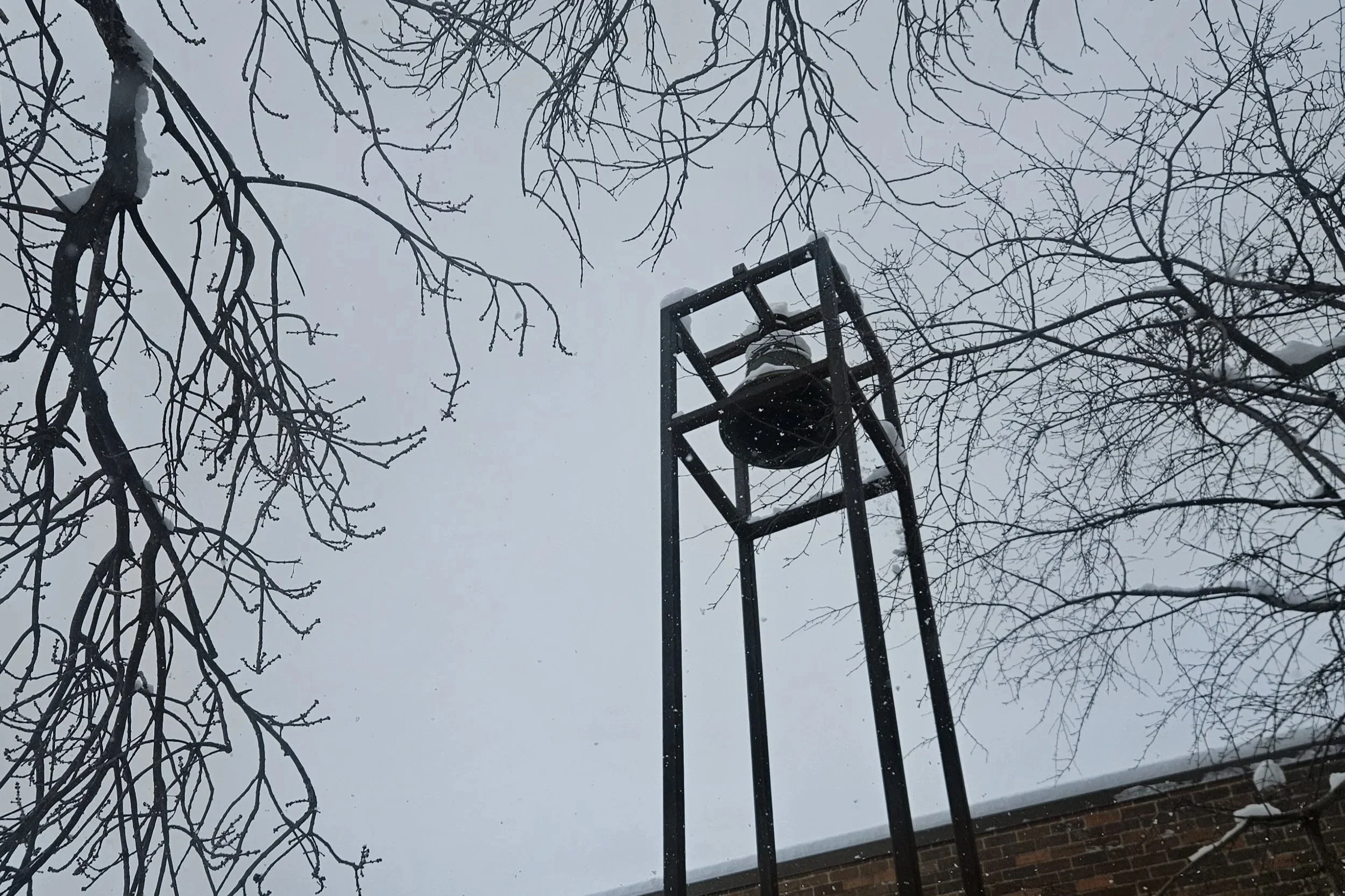 Snow-covered tree branches surround the original Church of the Three Crosses bell tower on a winter day.