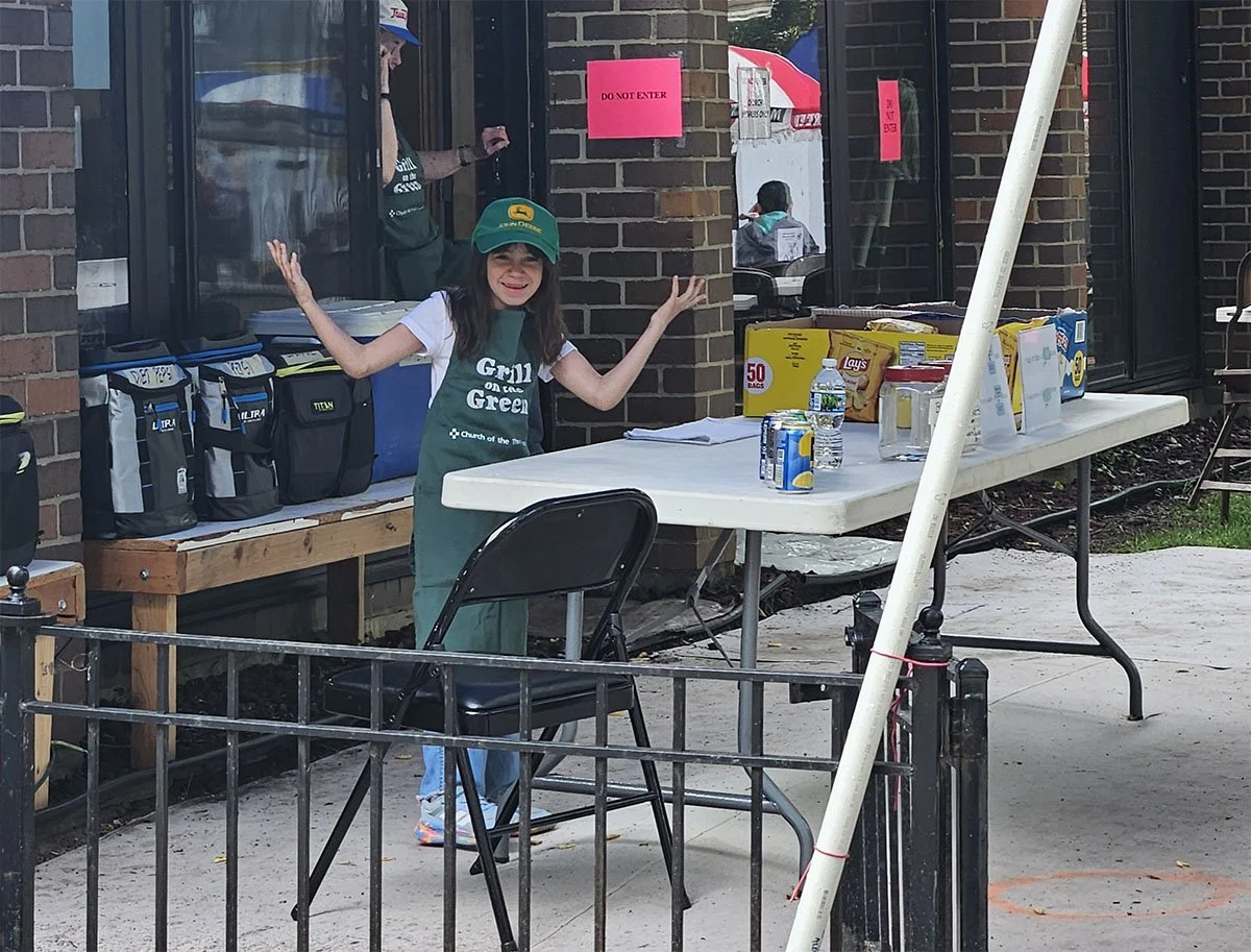 A kid shrugging while serving food at the Church of the Three Crosses Grill on the Green event during the Old Town Triangle Art Fair.