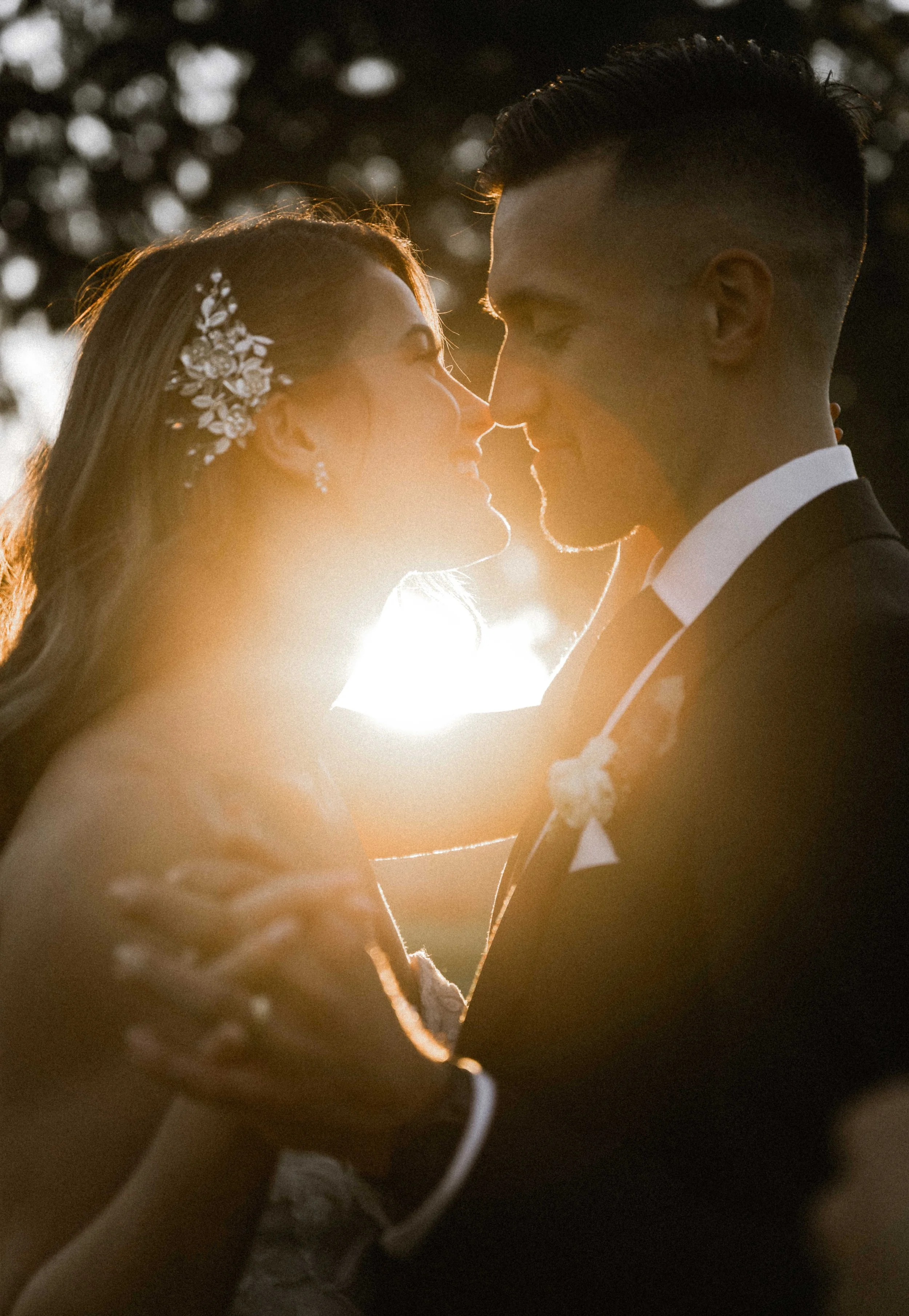 A bride and groom sharing a close, intimate moment at sunset with sunlight creating a glow around them.