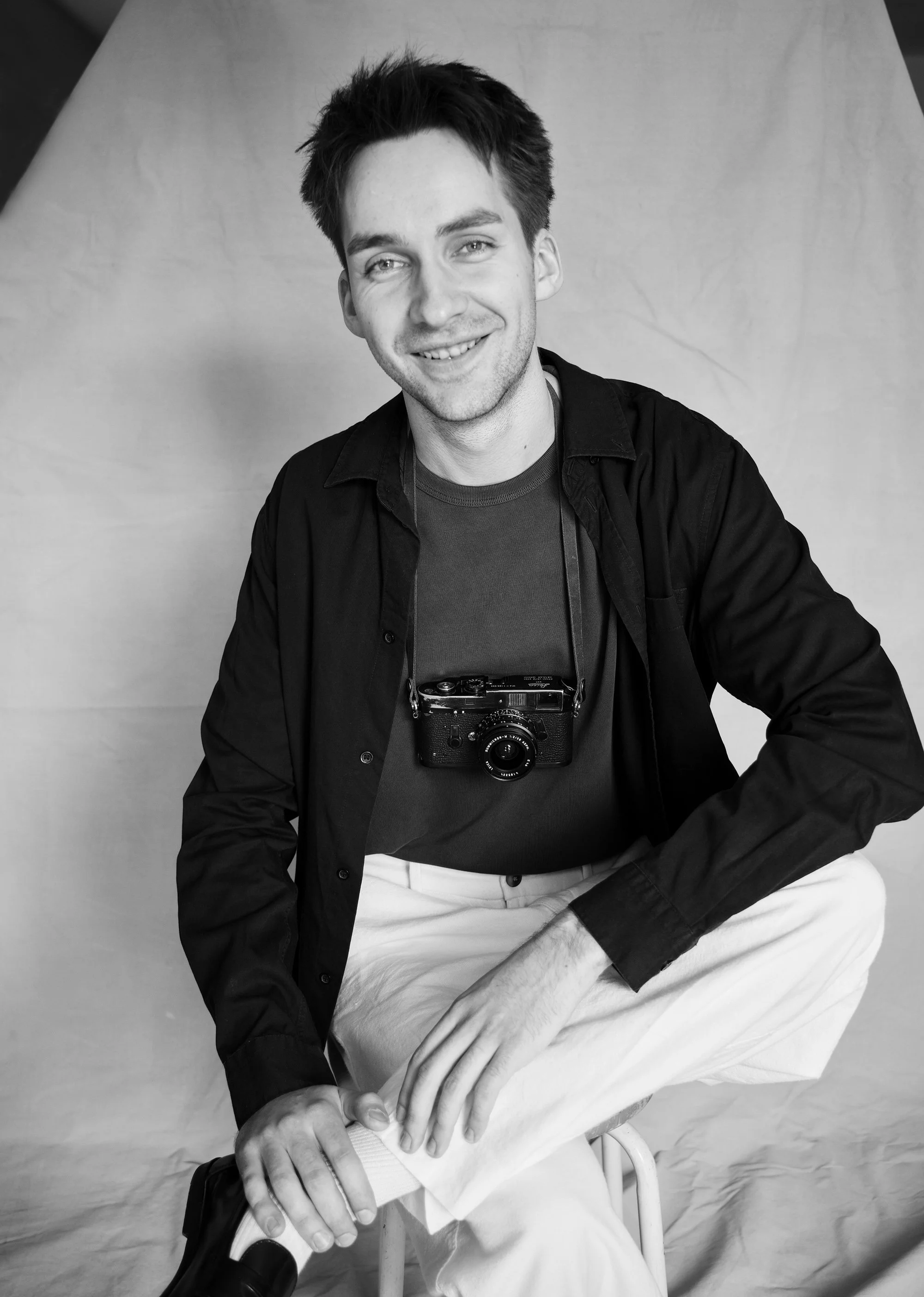 a black and white natural light portrait of a christian wedding photographer wearing a film camera around the neck