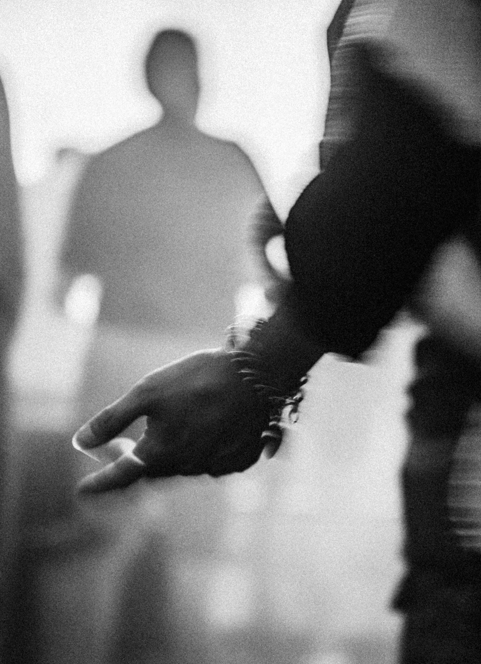 Black and white photo of a person's hand extended in worship, with a man standing in the background, slightly out of focus.