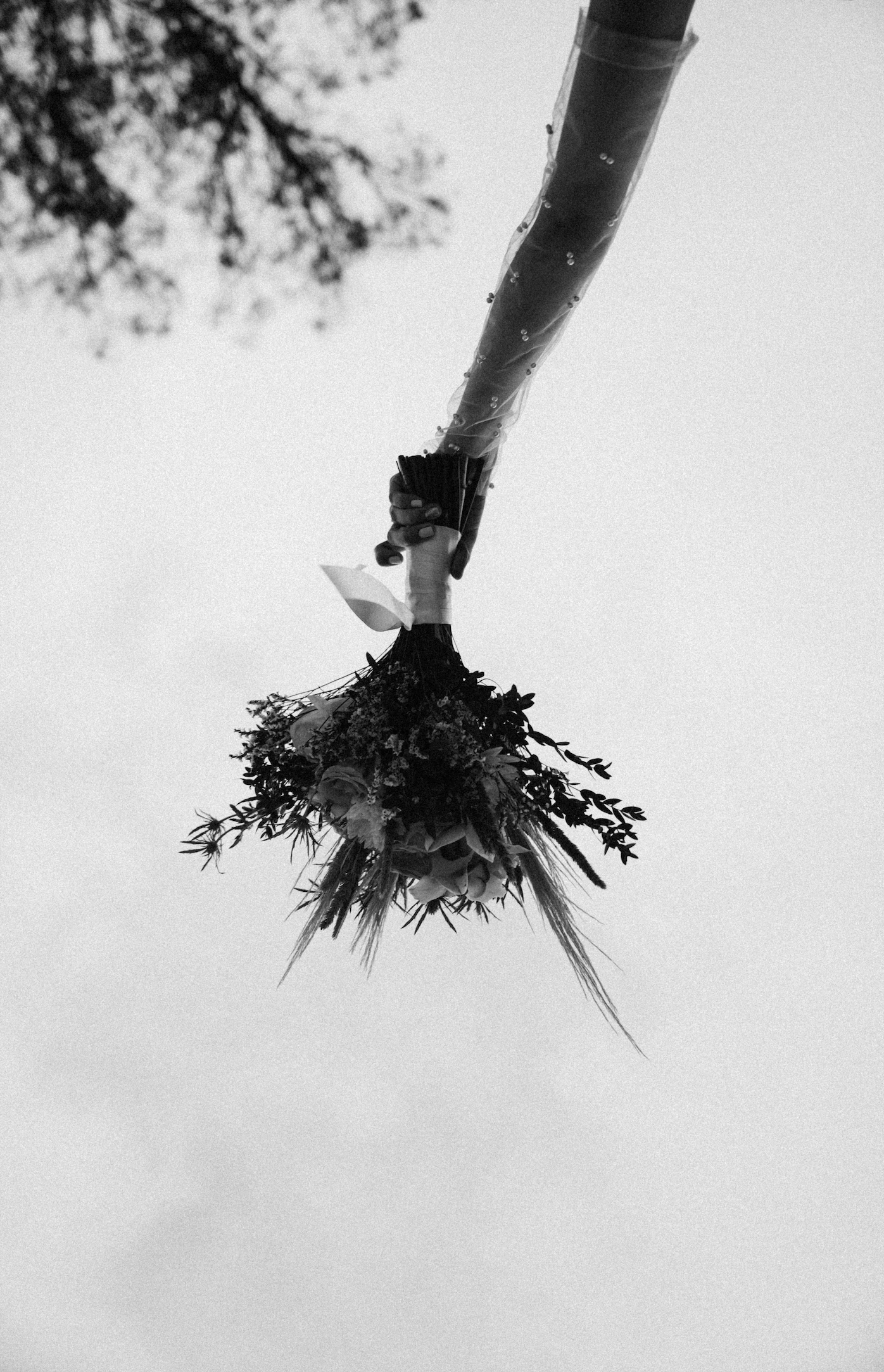A black and white photo of a bouquet of flowers being held upside down against the sky, with a hand gripping the bouquet.