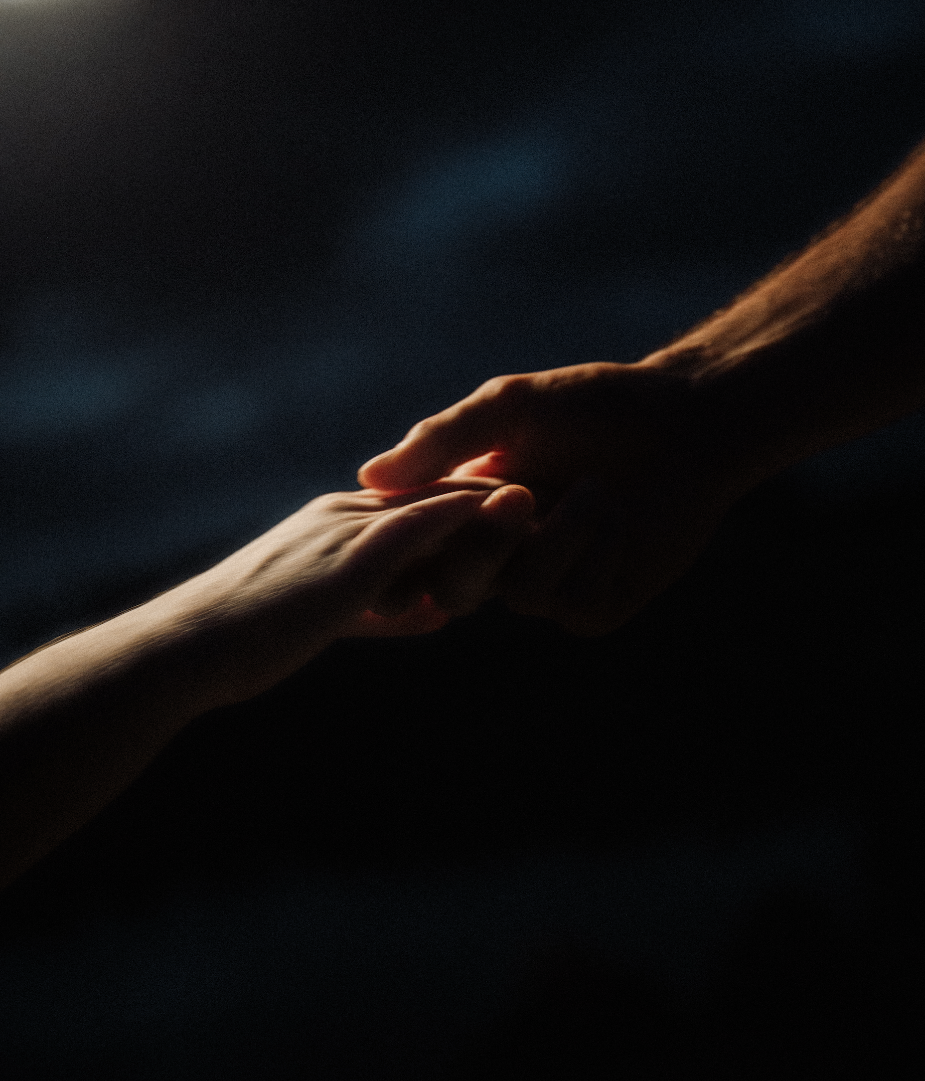 Two hands reaching out and holding each other in a dark background.