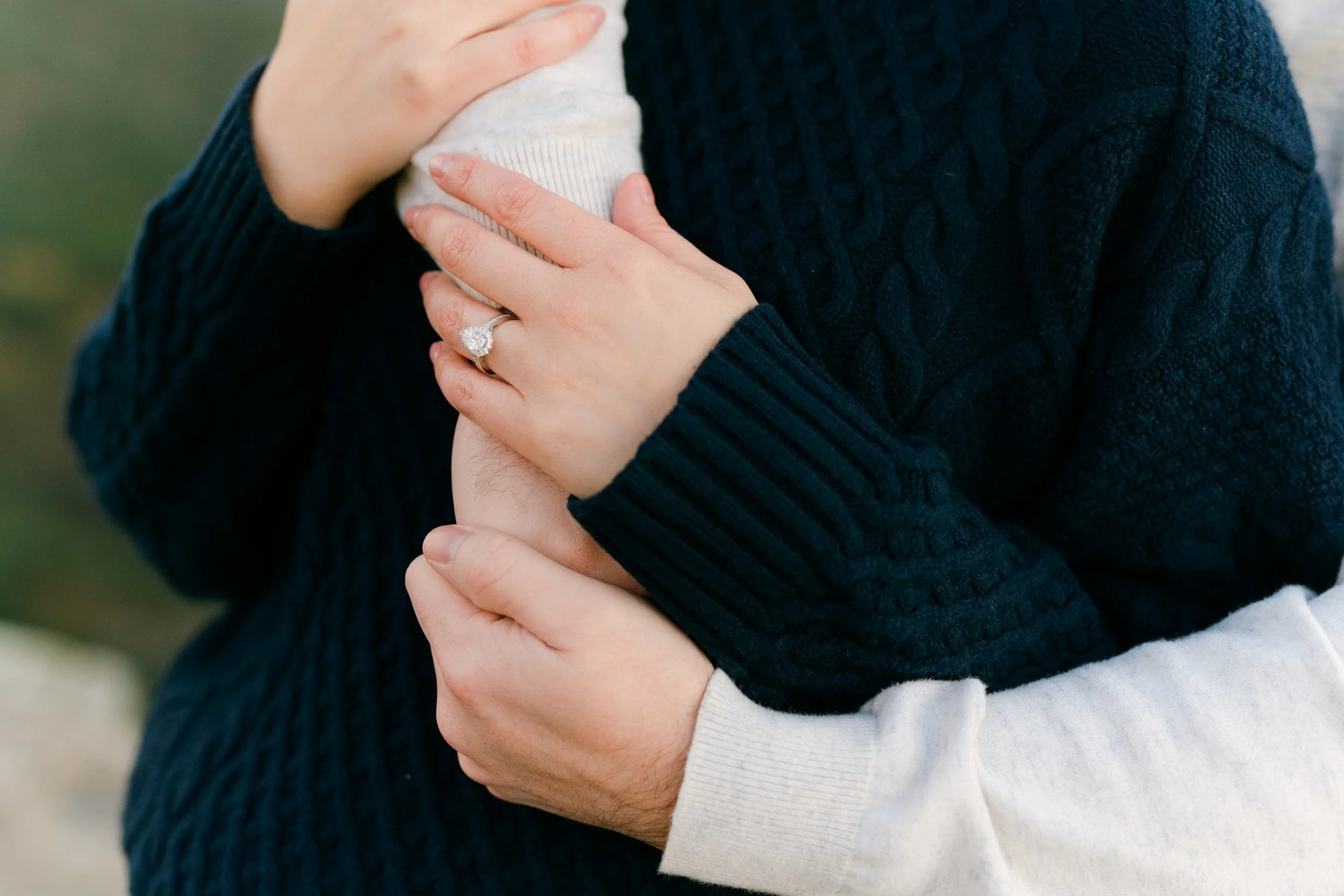 A close up of a couple embracing, one with a diamond engagement ring, both wearing sweaters, after choosing one of the best places to propose colorado, Lost Gulch Overlook in Boulder Colorado.