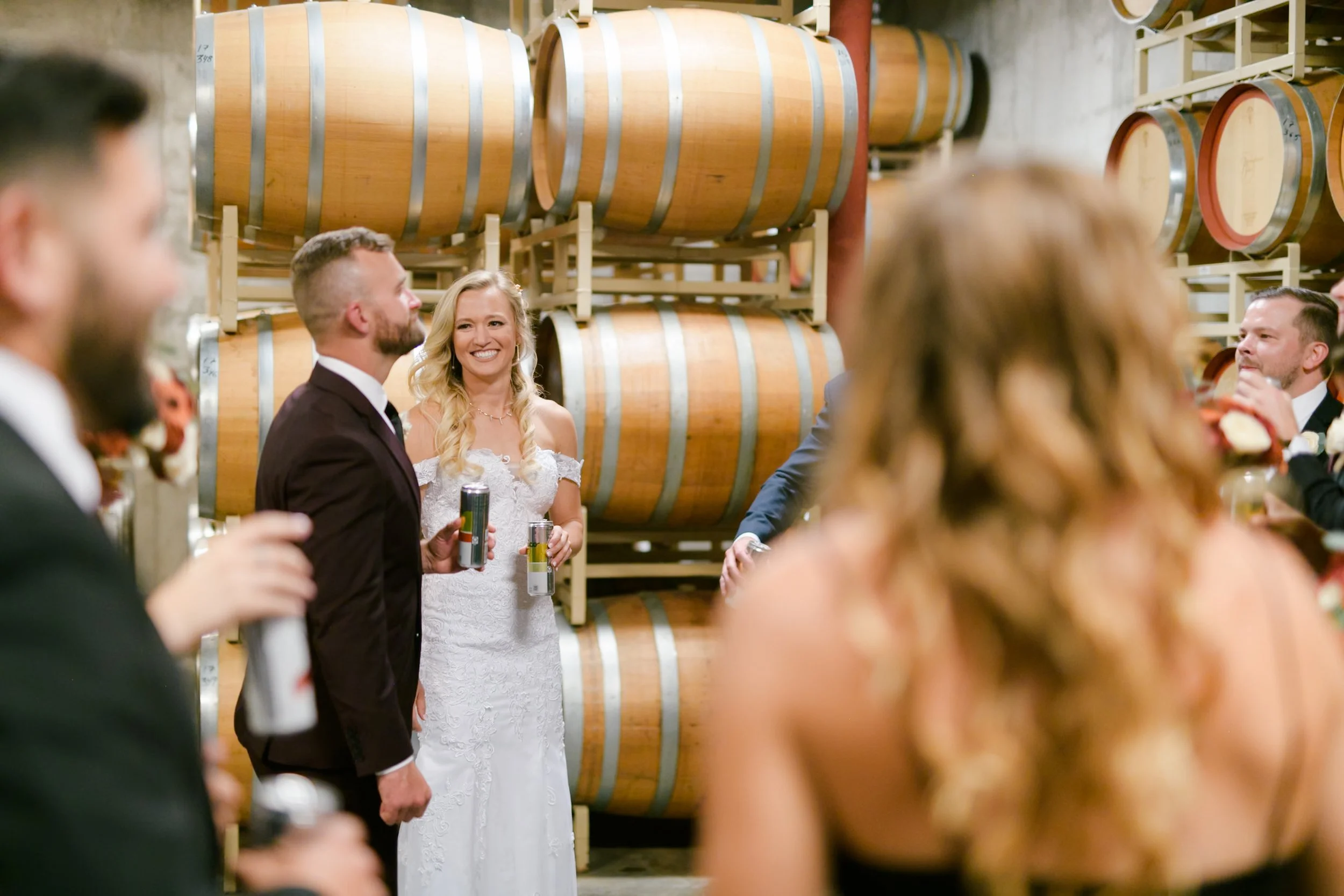 A bride and groom laugh in the basement of Balestri surrounded by barrels of wine
