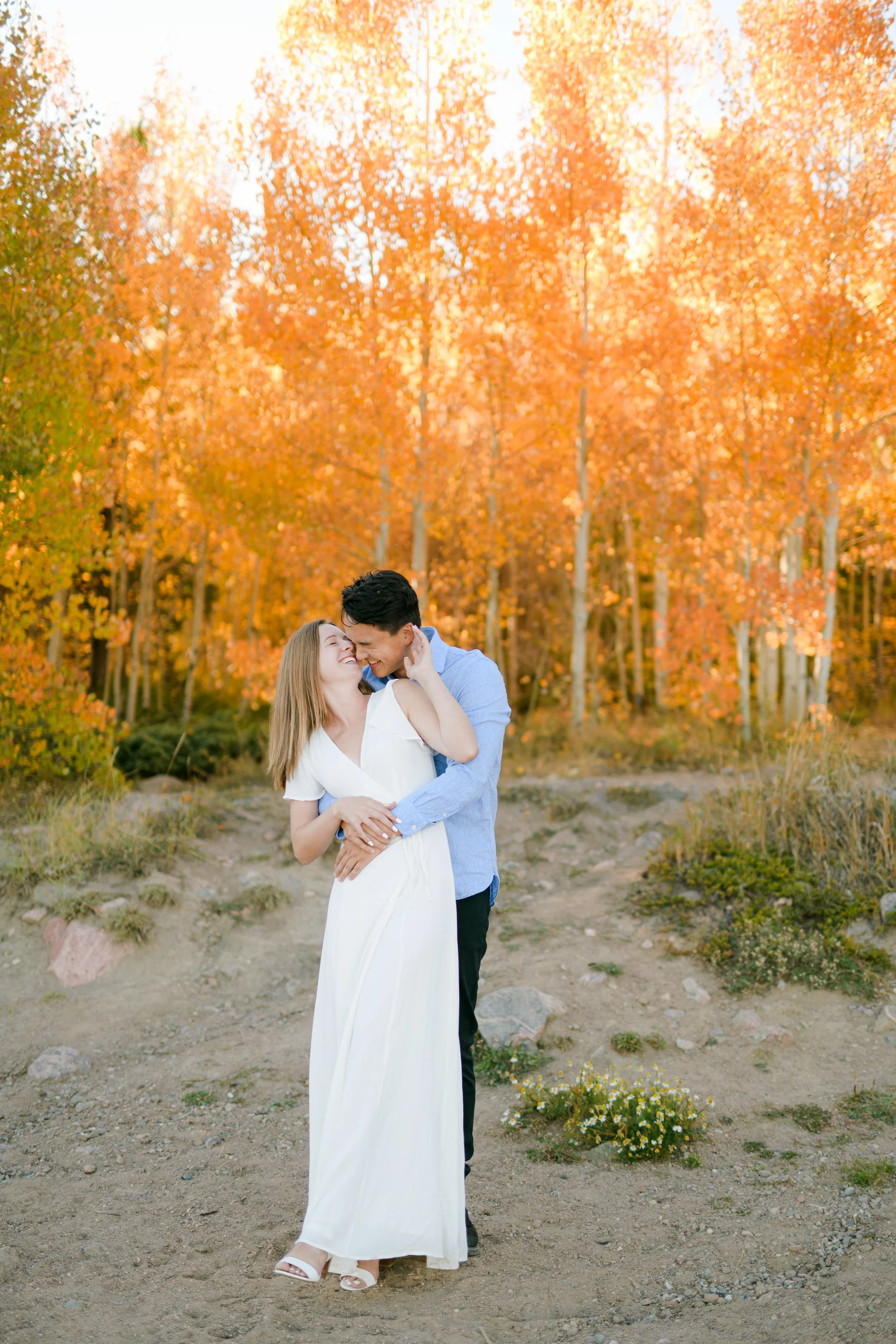 A couple embracing and smiling in a forest with orange fall foliage near a lake dillon engagement session in Frisco, Colorado