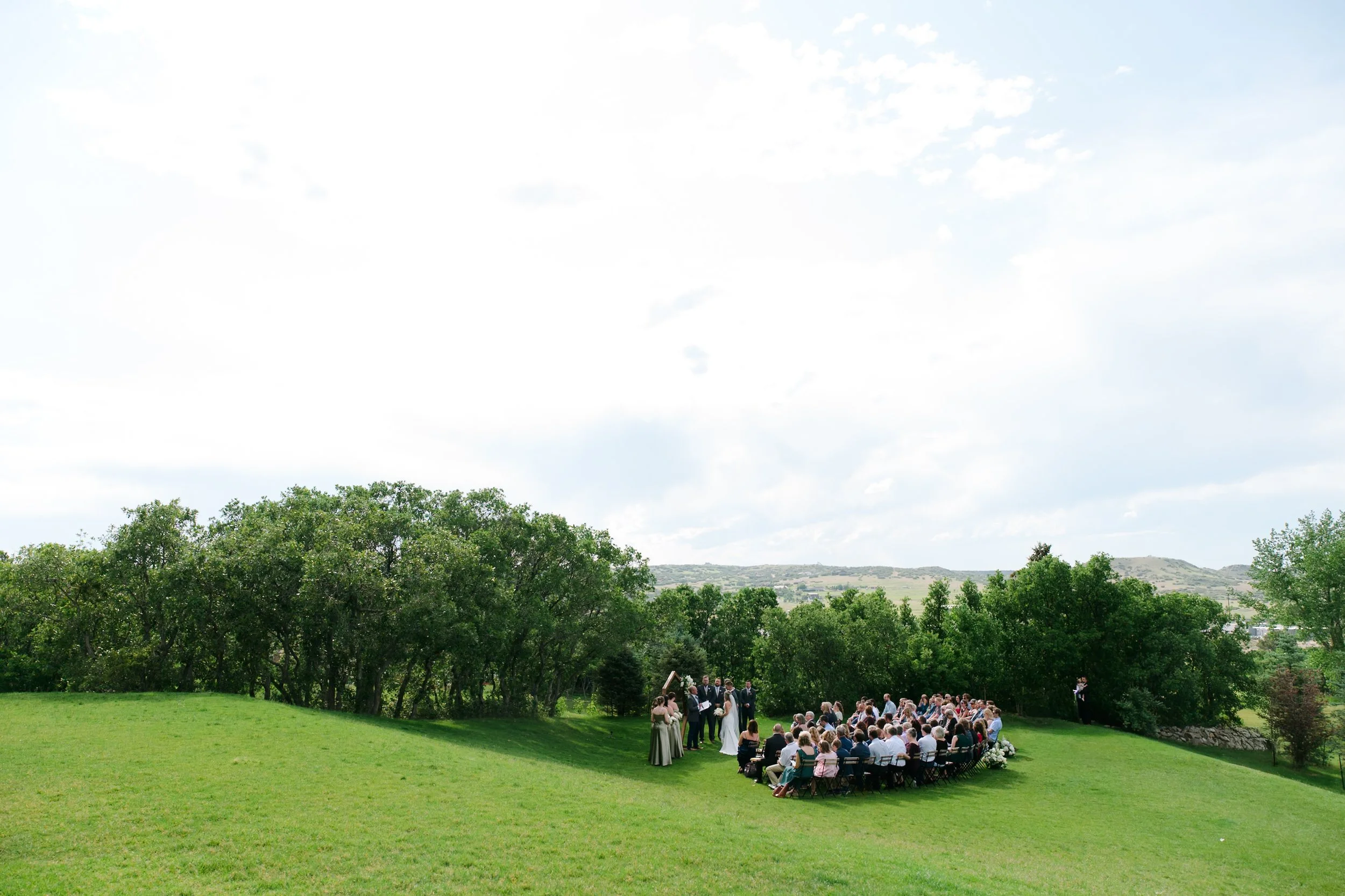 a wedding at the oaks in castle rock with green grass, a blue sky, and the people very small in the bottom right