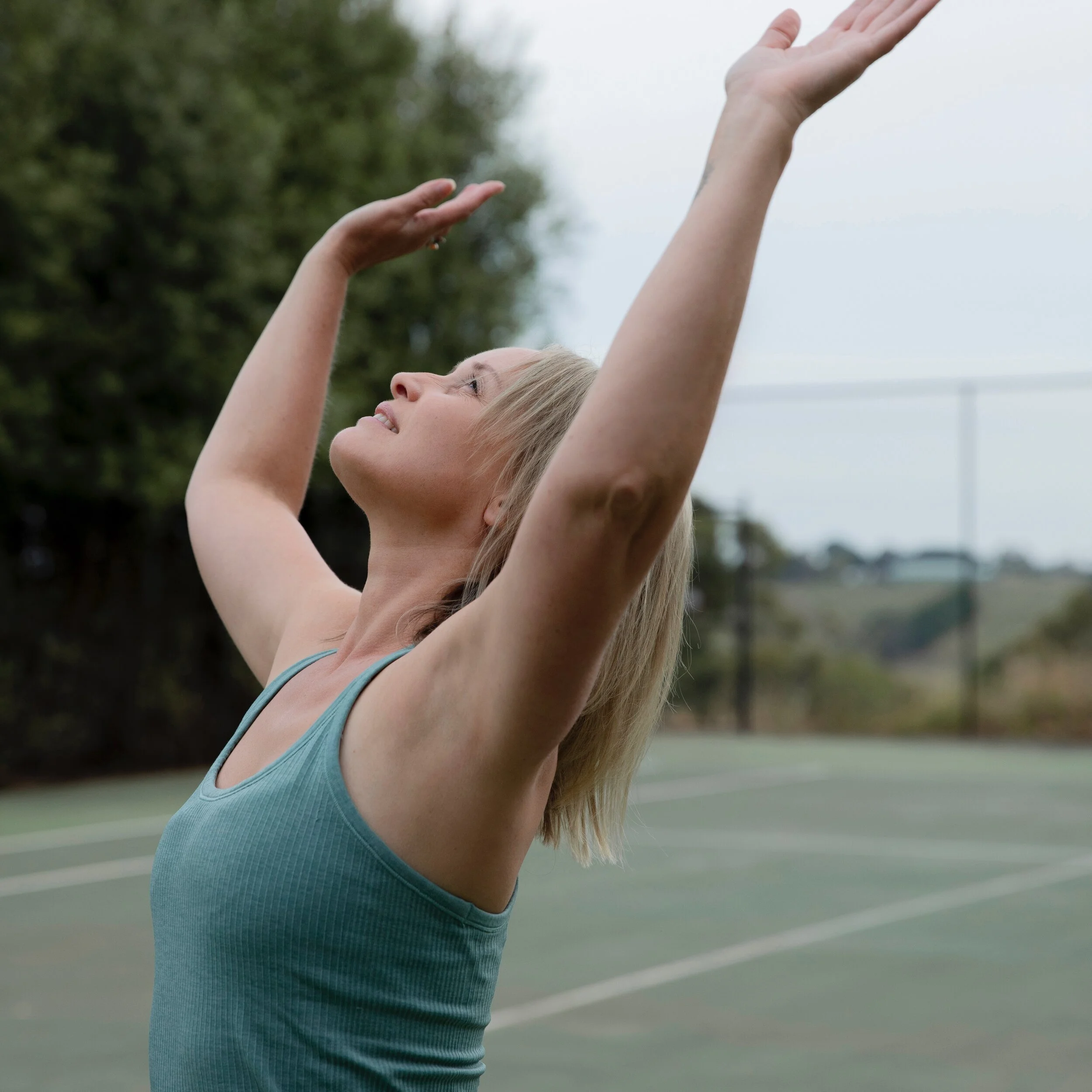 Nicole Lee practicing Qigong outdoors with arms raised in an expansive movement posture