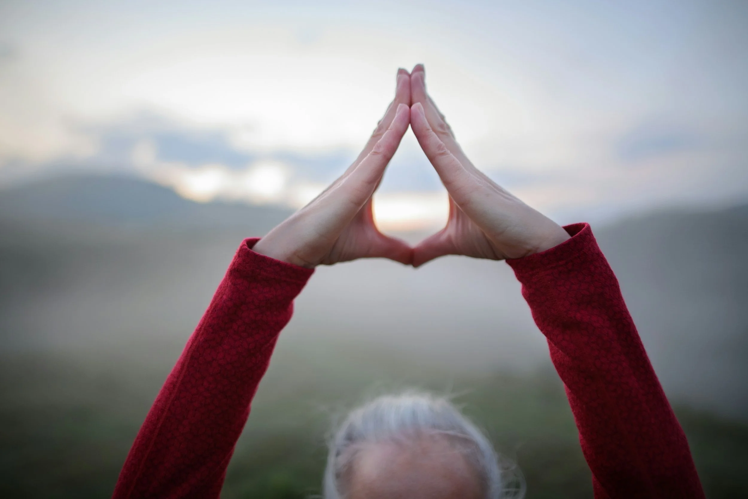 Person holding their hands in a triangular Qigong posture outdoors at sunrise, symbolising embodied practice, internal cultivation and energetic awareness.