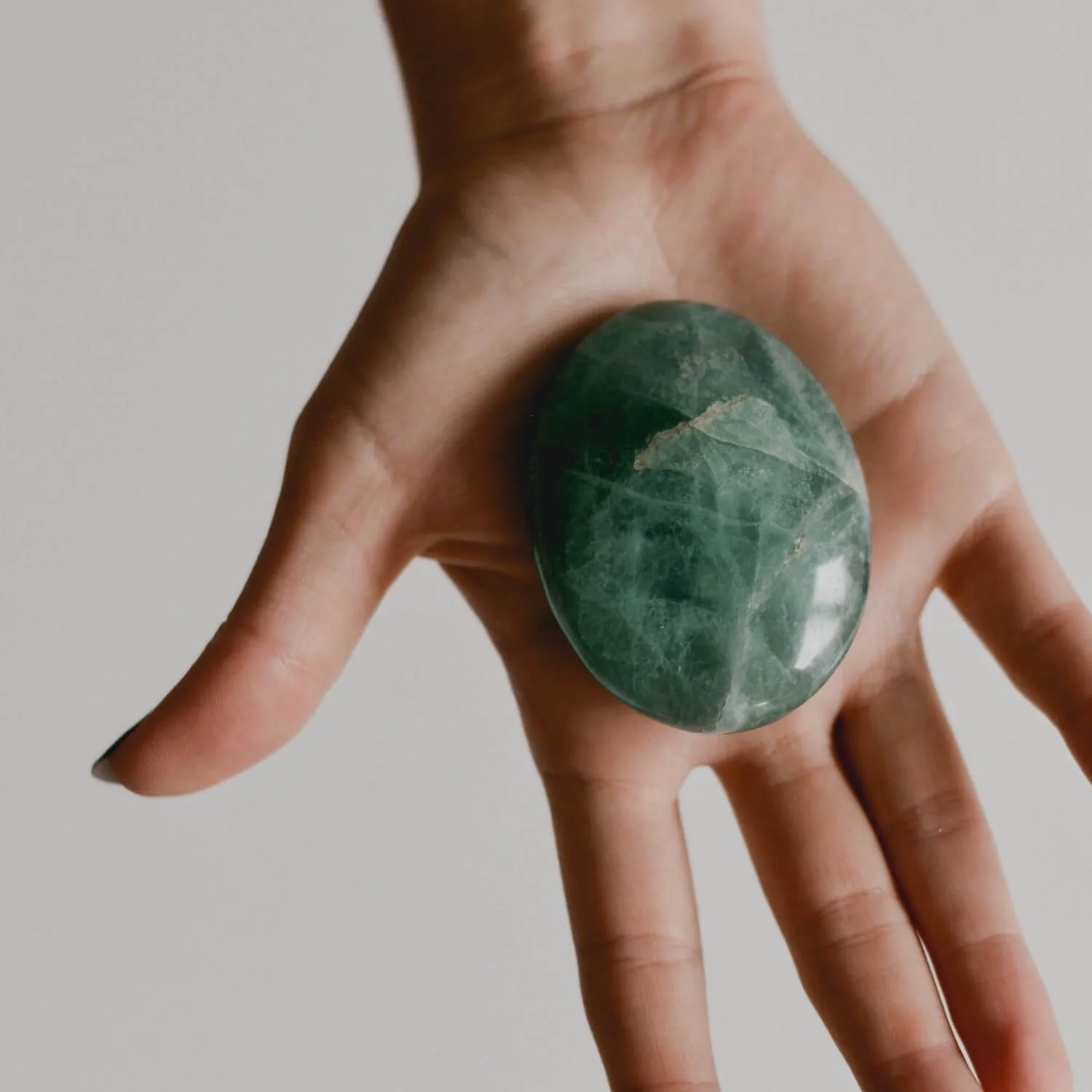 Hand holding a polished green stone, shown in close-up against a neutral background