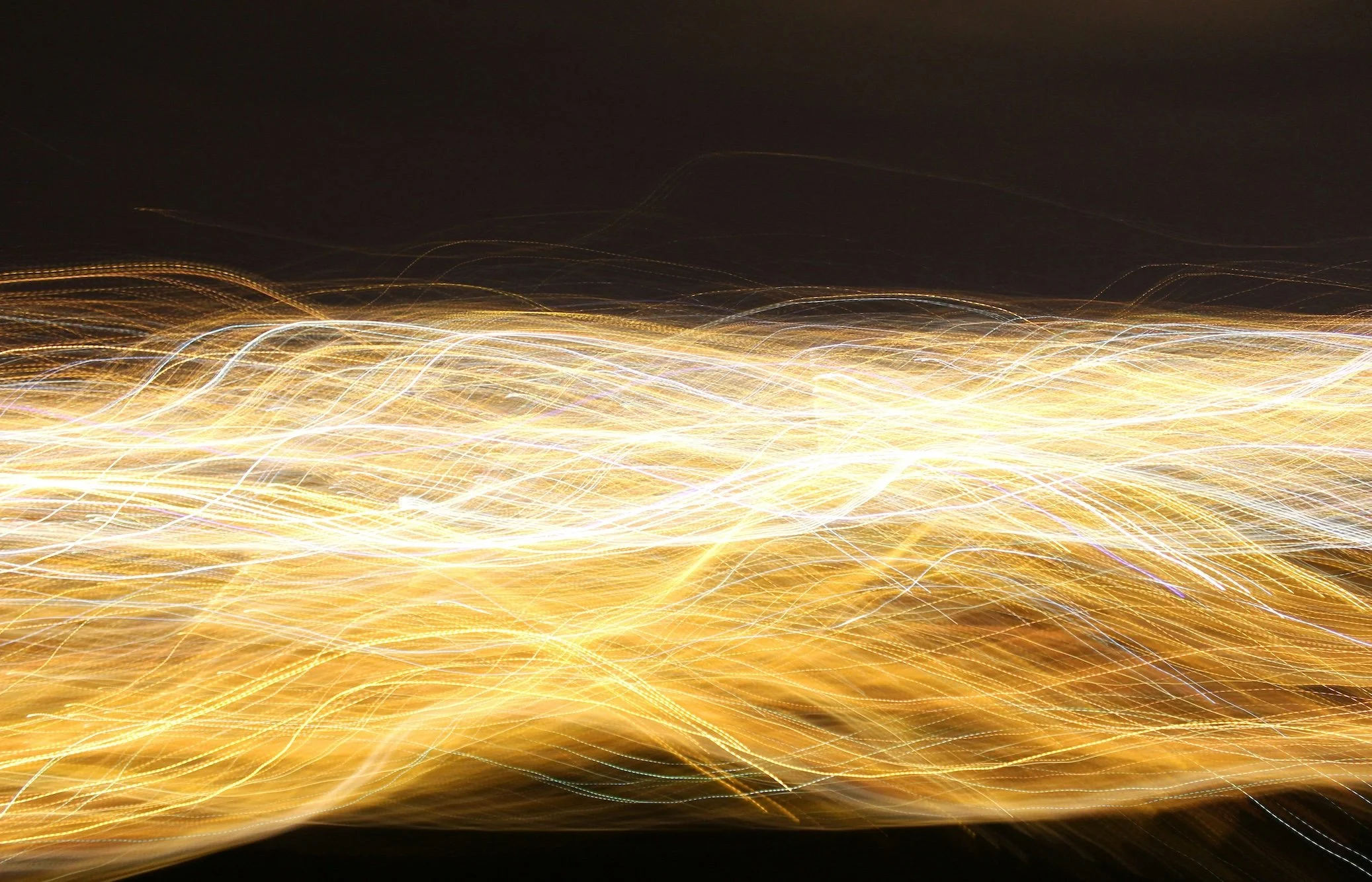 Abstract image of flowing golden and white light trails against a dark background.