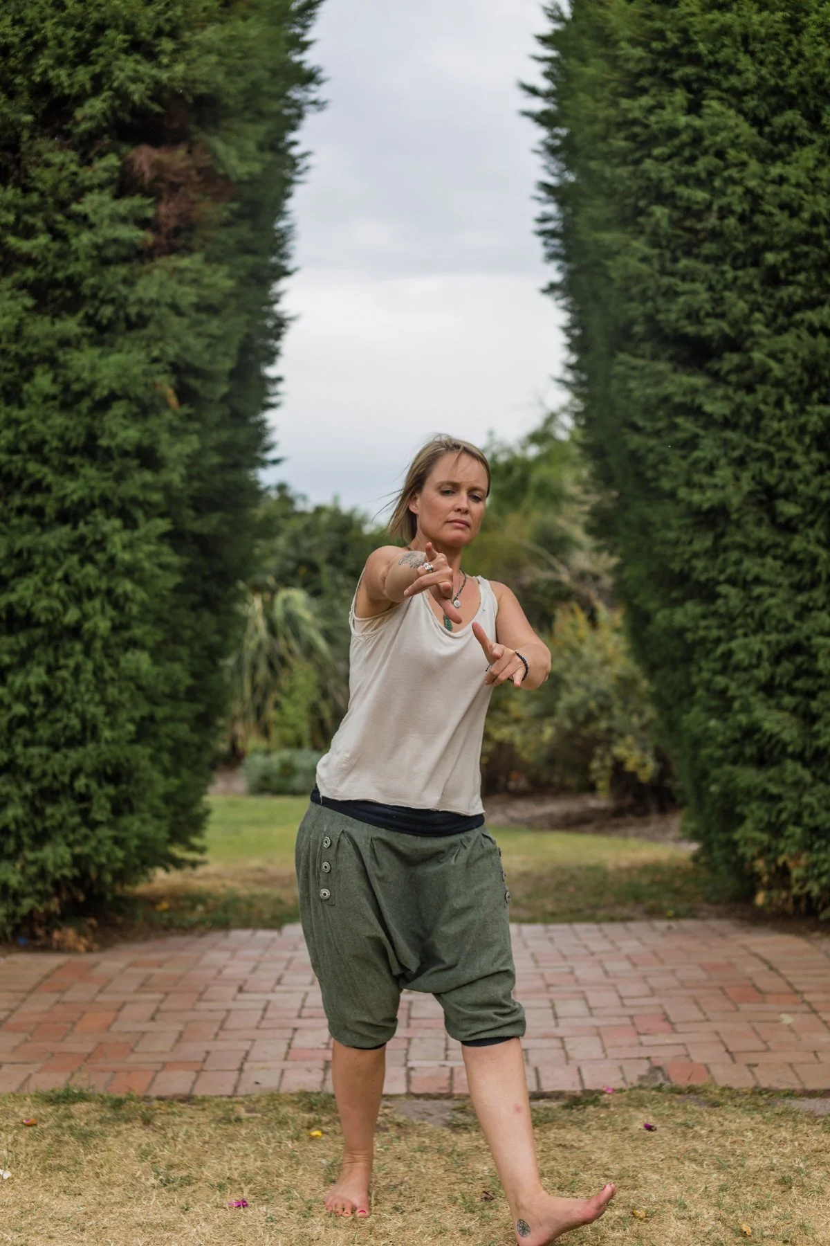 Woman practising Five Animal Frolics Qigong outdoors, demonstrating an animal-inspired movement in a garden setting.