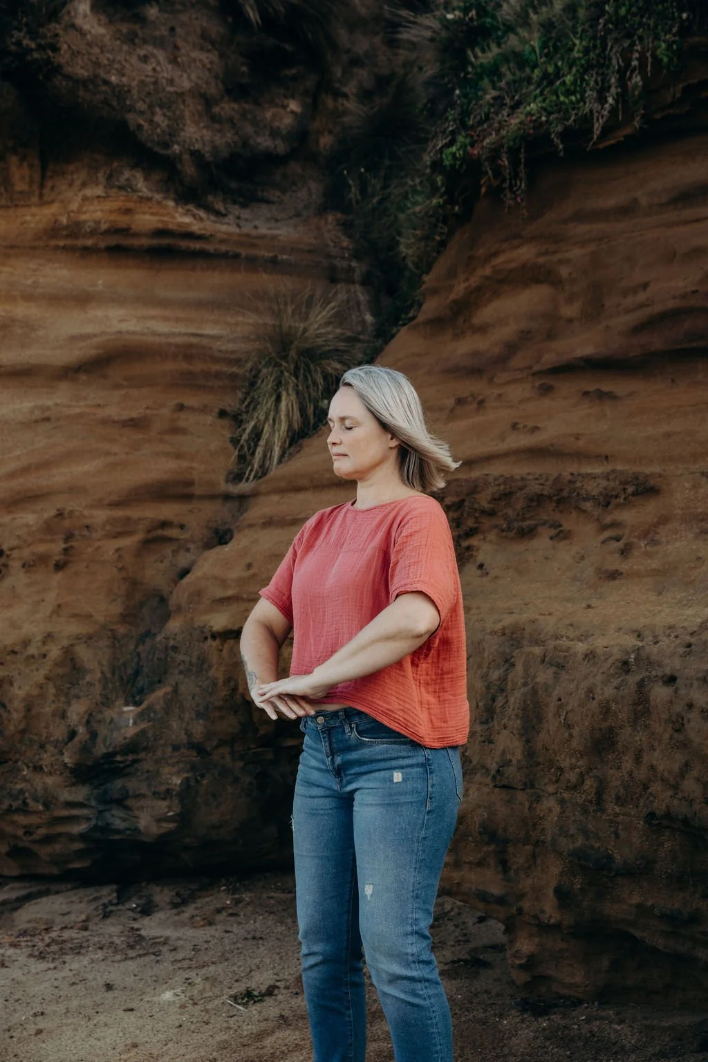Woman practising a seated Celestial Shen Gong Qigong form outdoors, with hands held at the lower abdomen and eyes gently closed.