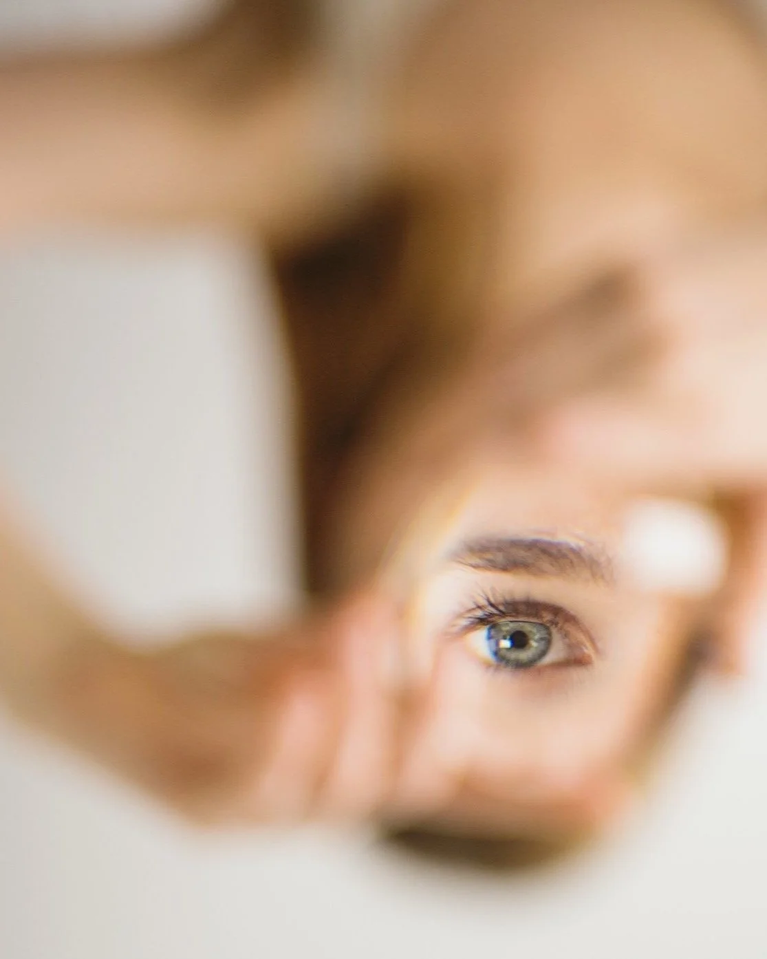 Close-up portrait of a person looking through their hands, representing deeper awareness of the Self and inner experience.