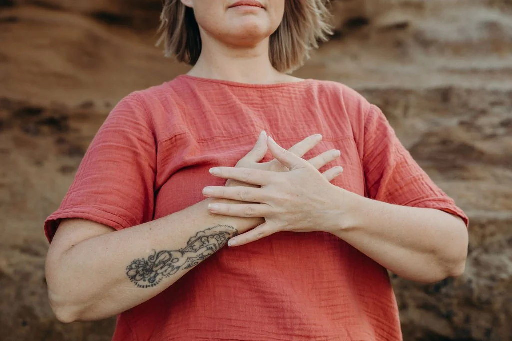 Person standing outdoors with both hands resting over the heart