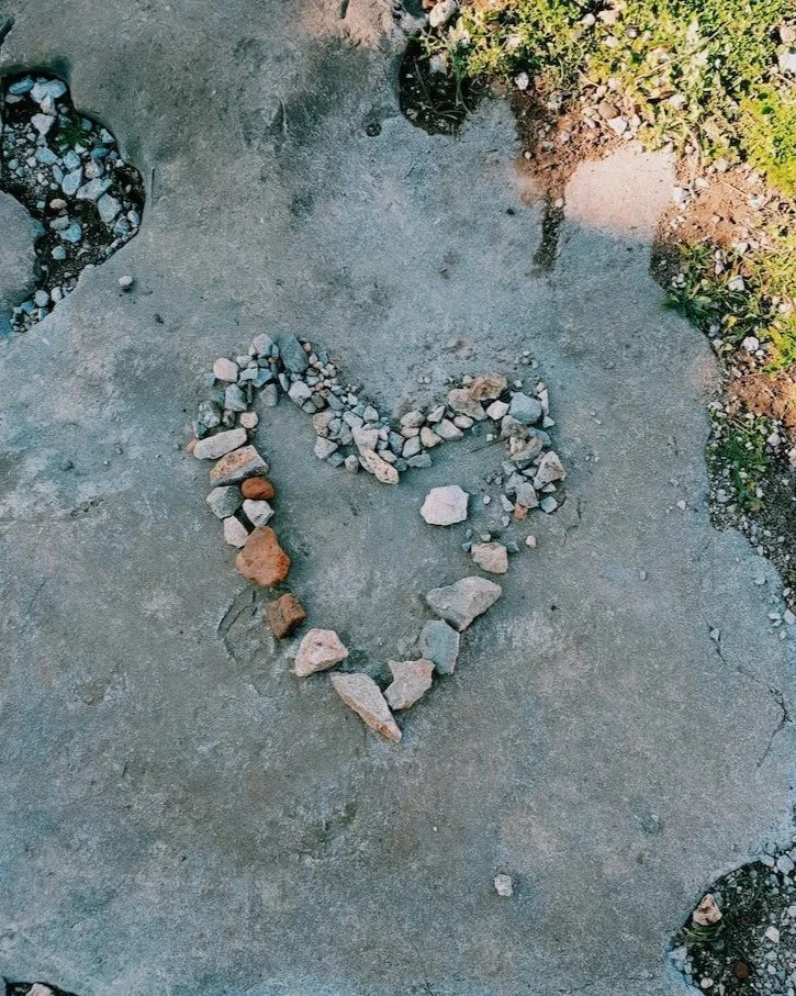 Small natural stones arranged in the shape of a heart on a stone surface.