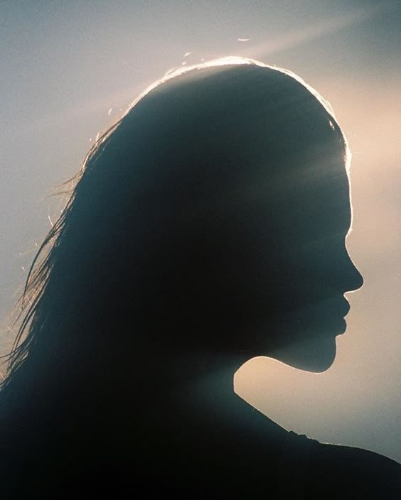 Silhouette of a woman with wet hair against a backlit sky.