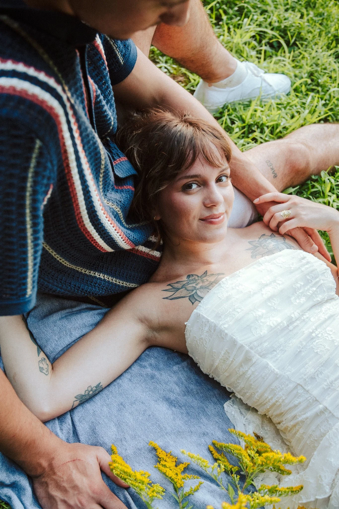 A person laying on their partner's lap as they sit in the grass 