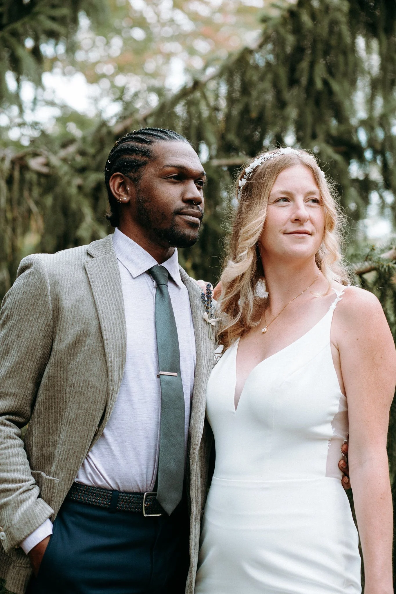 A newlywed couple with their arms around each other looking off into the distance 