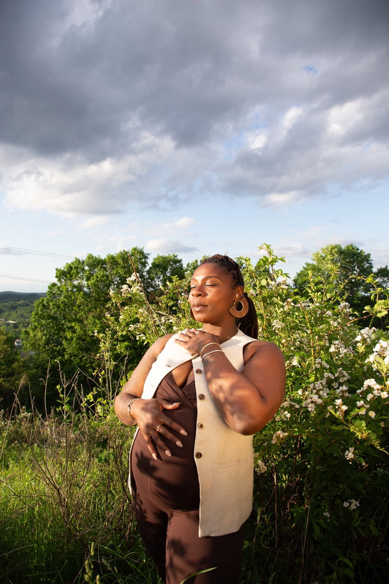 A pregnant person with on hand on their stomach and their eyes closed 