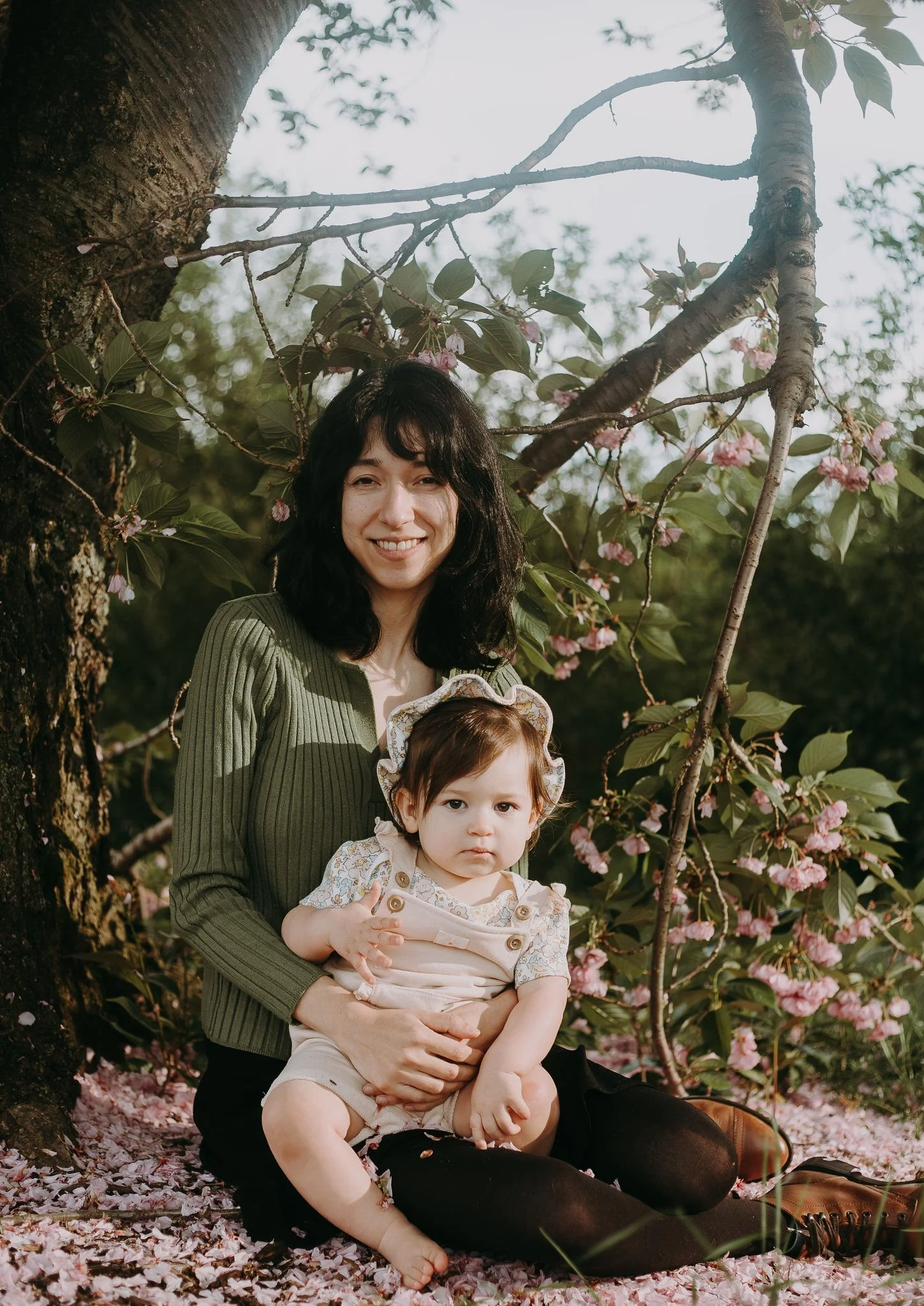 A parent sitting in front of a tree with their child in their lap