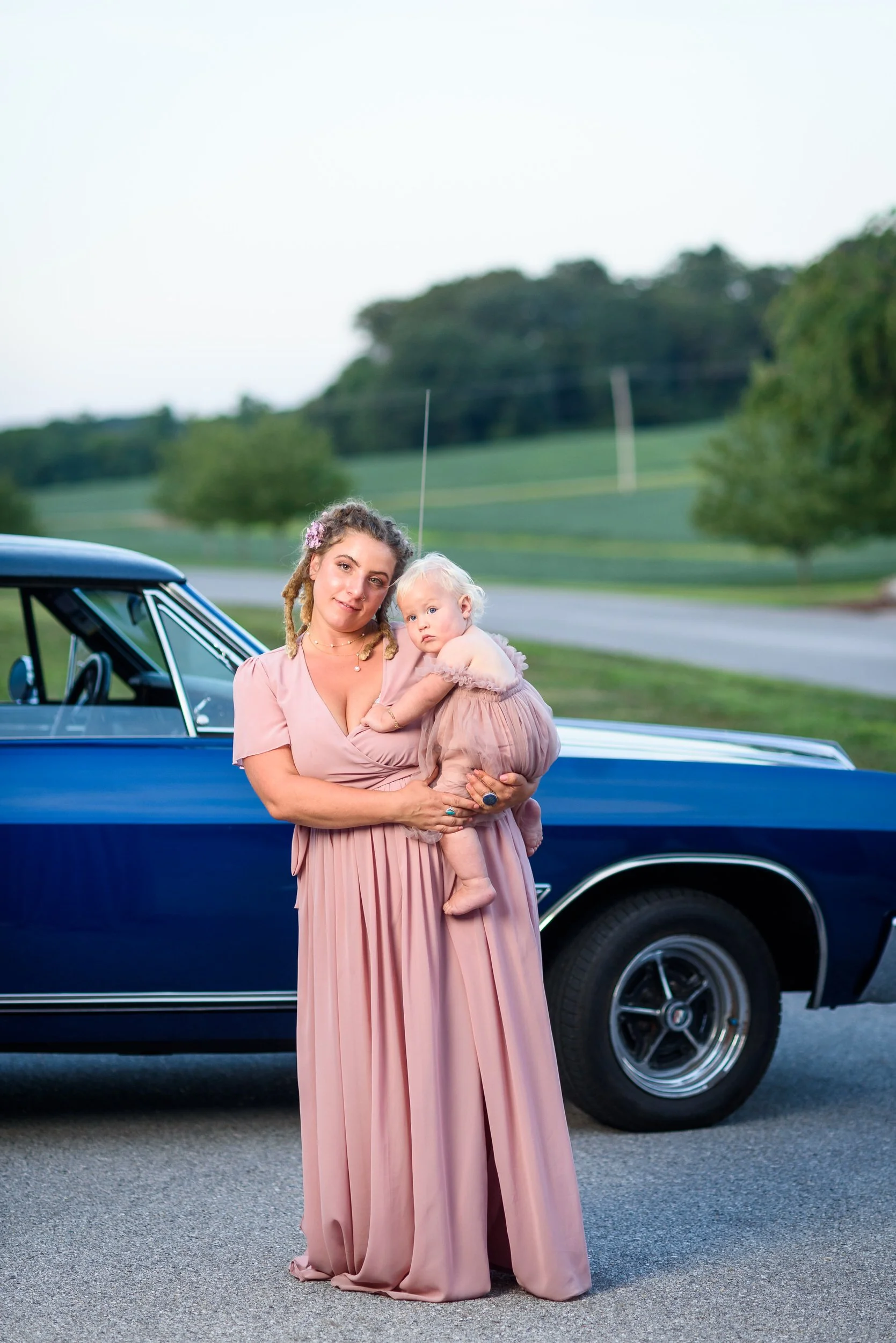A mother holding their baby while standing in front of a classic car