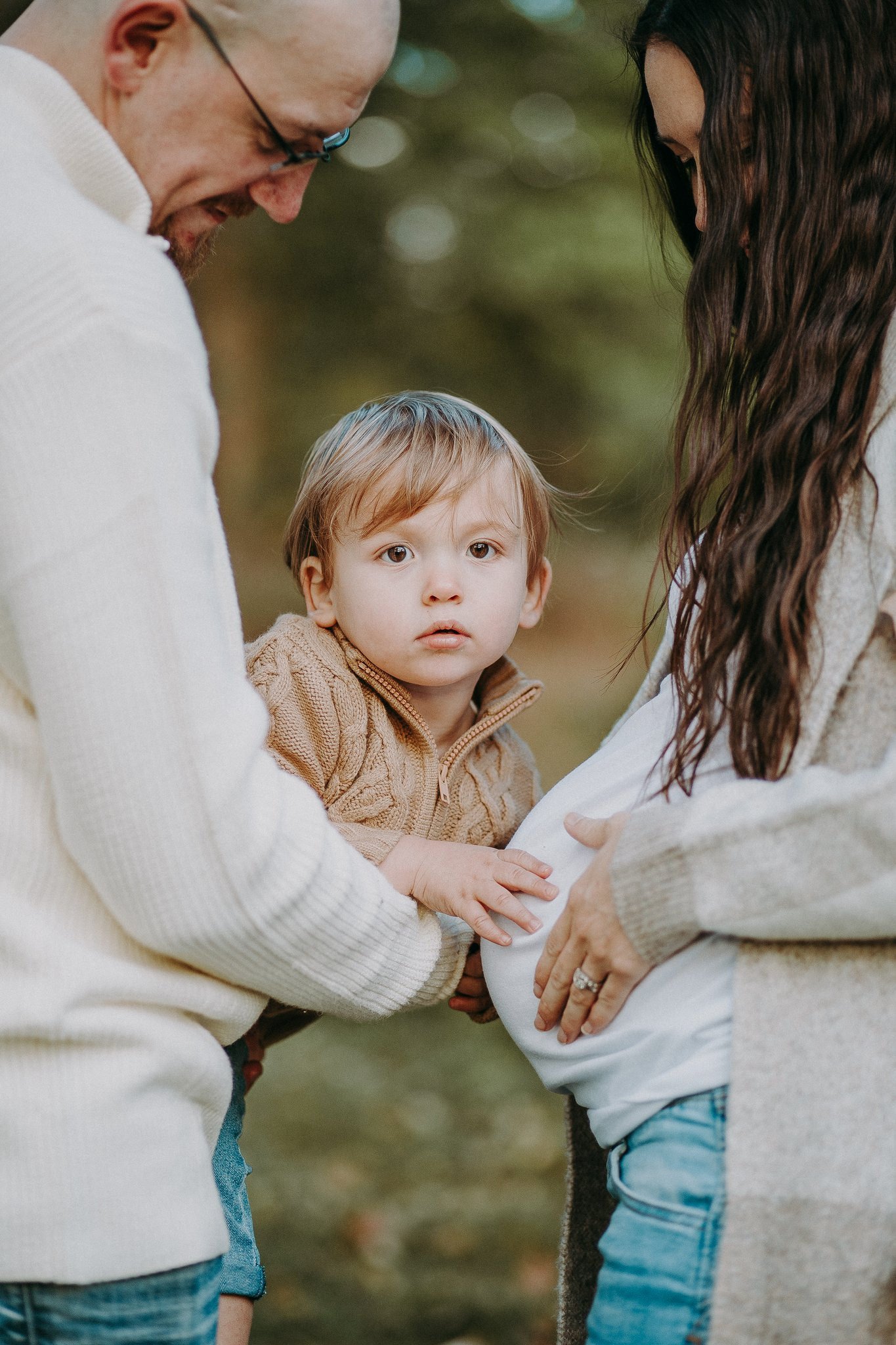 A parent holding a small child as they reach out to their mom's pregnant stomach 