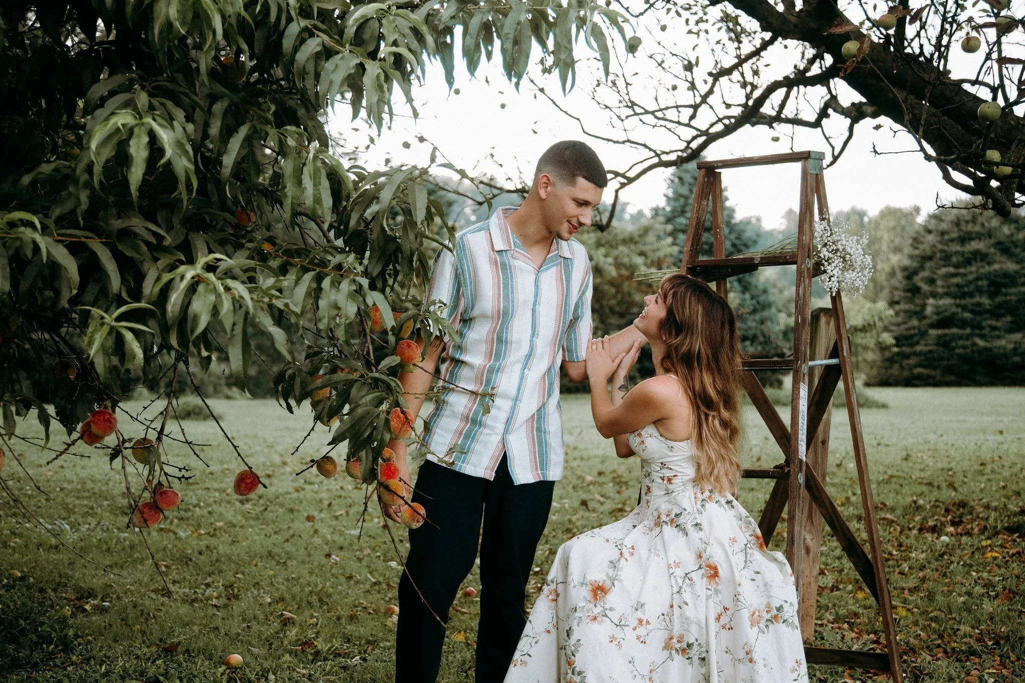 A person reaching towards their partner's face who is sitting on a ladder 