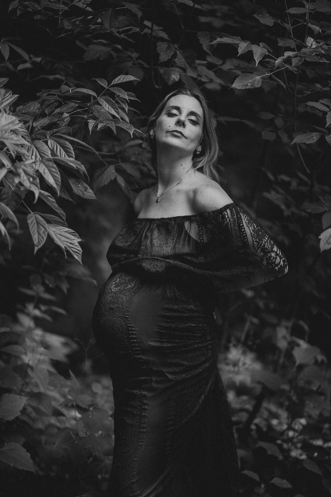 A pregnant person in a lace dress standing in the woods 