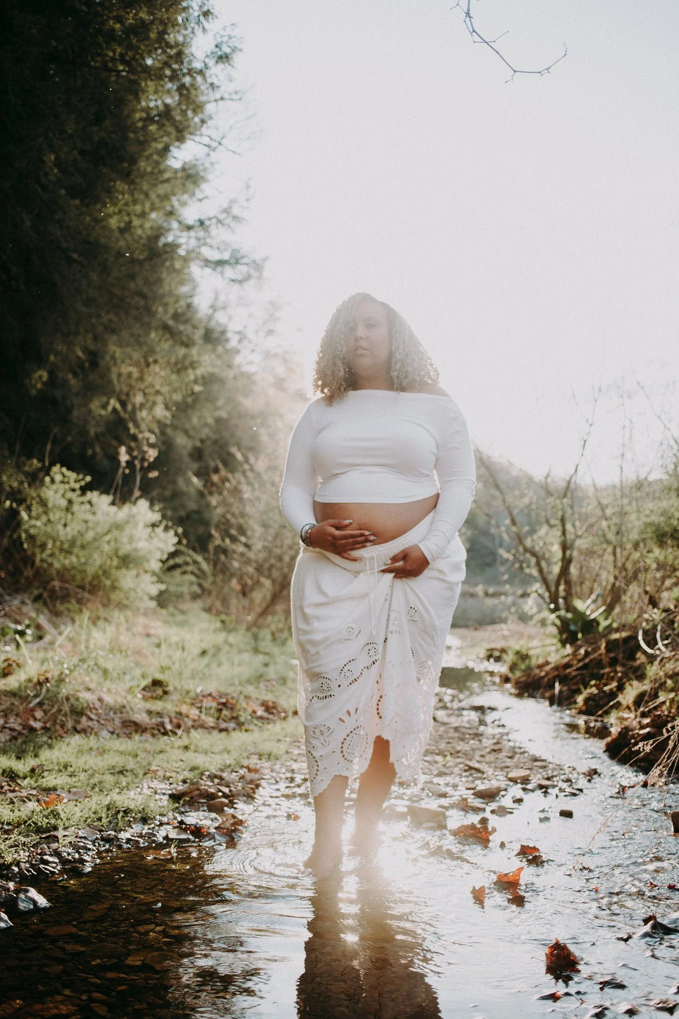 A pregnant person walking in a shallow creek 