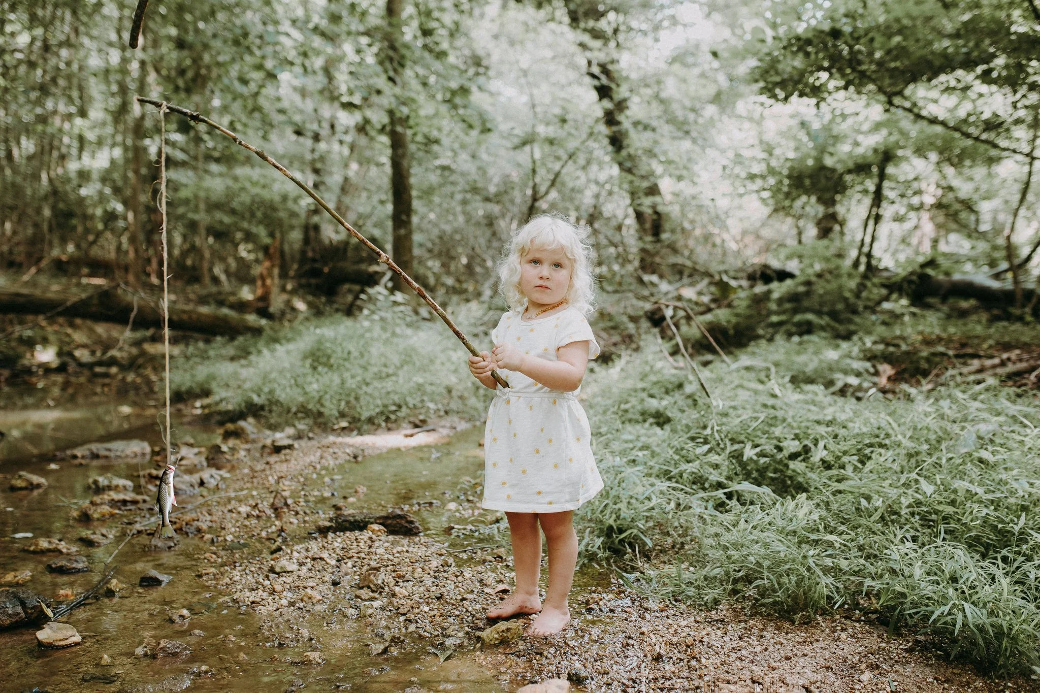 A child standing next to a creek holding a fishing pole