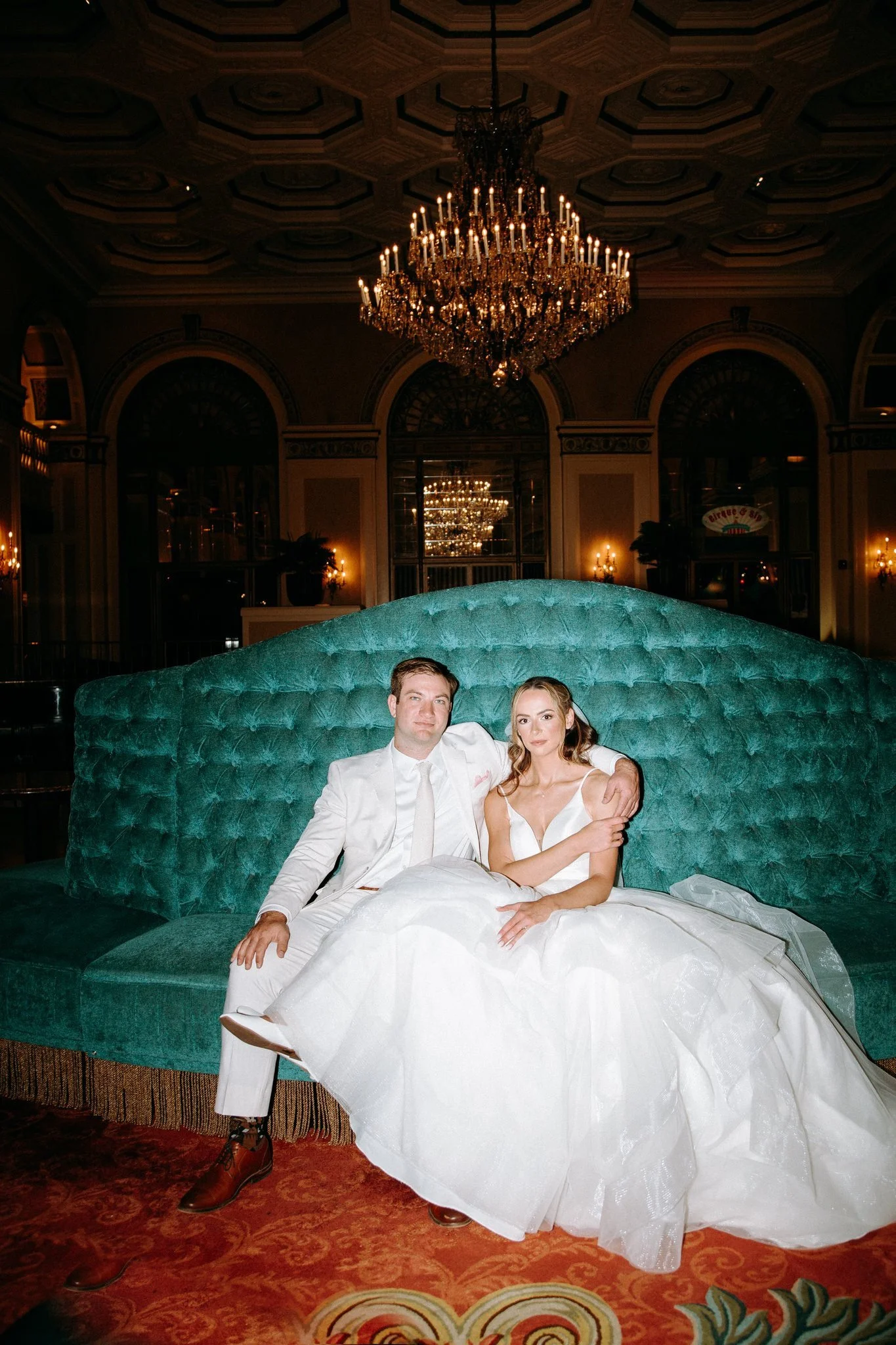 A newlywed couple sitting down on a large teal covered couch