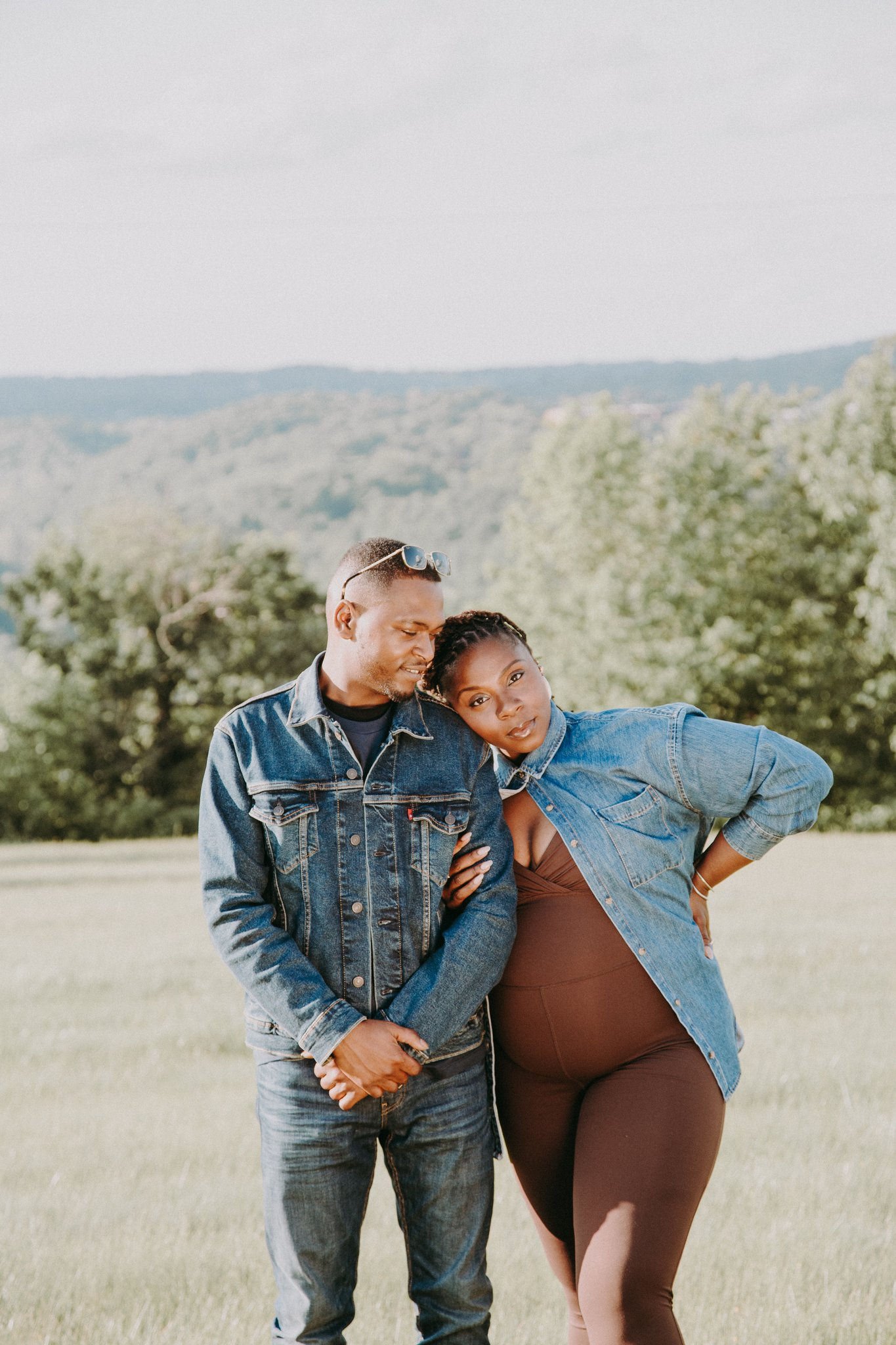 A pregnant couple with their arms linked standing in a field