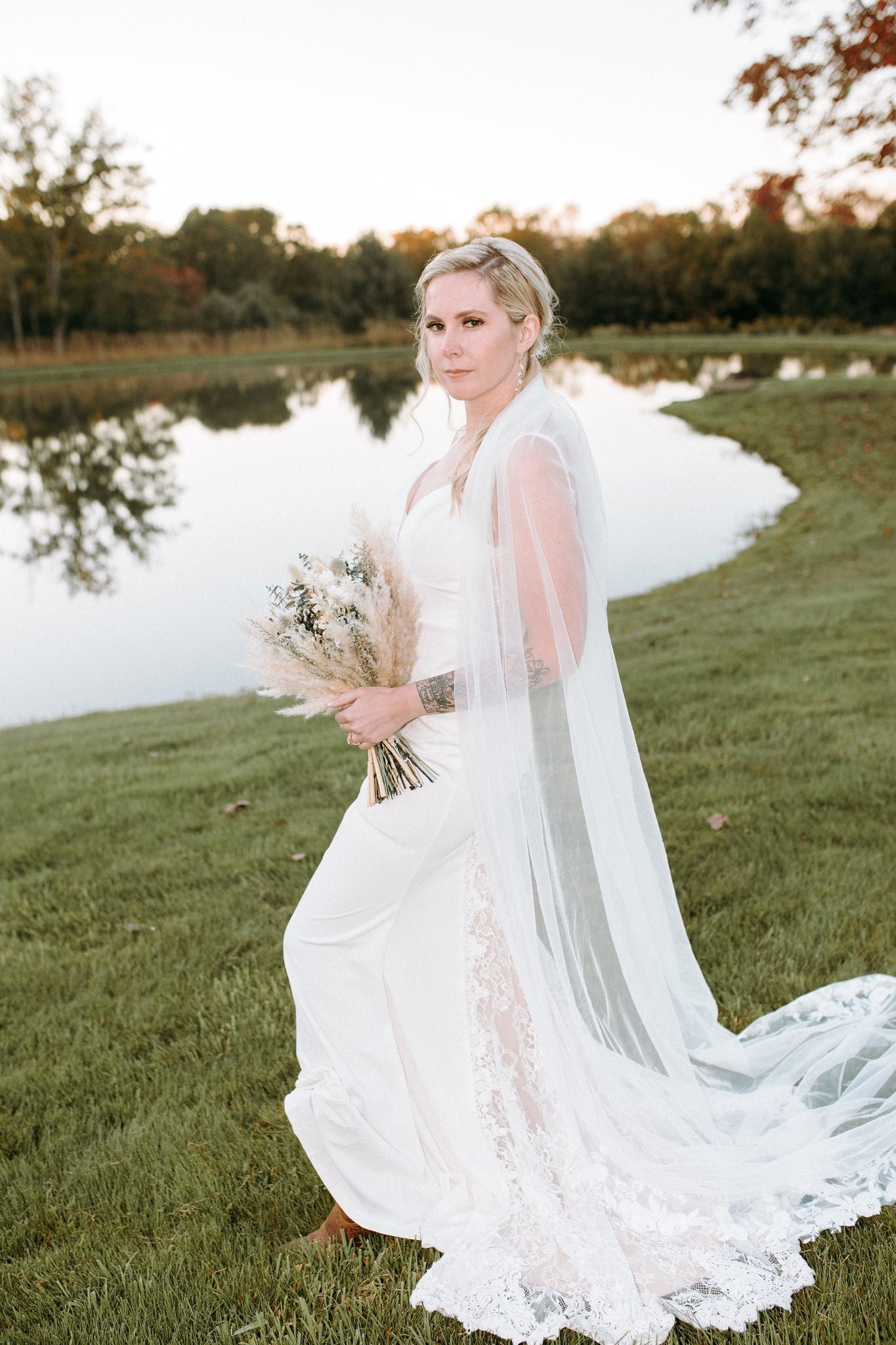A person in a wedding dress holding a bouquet of flowers and standing next to a lake 