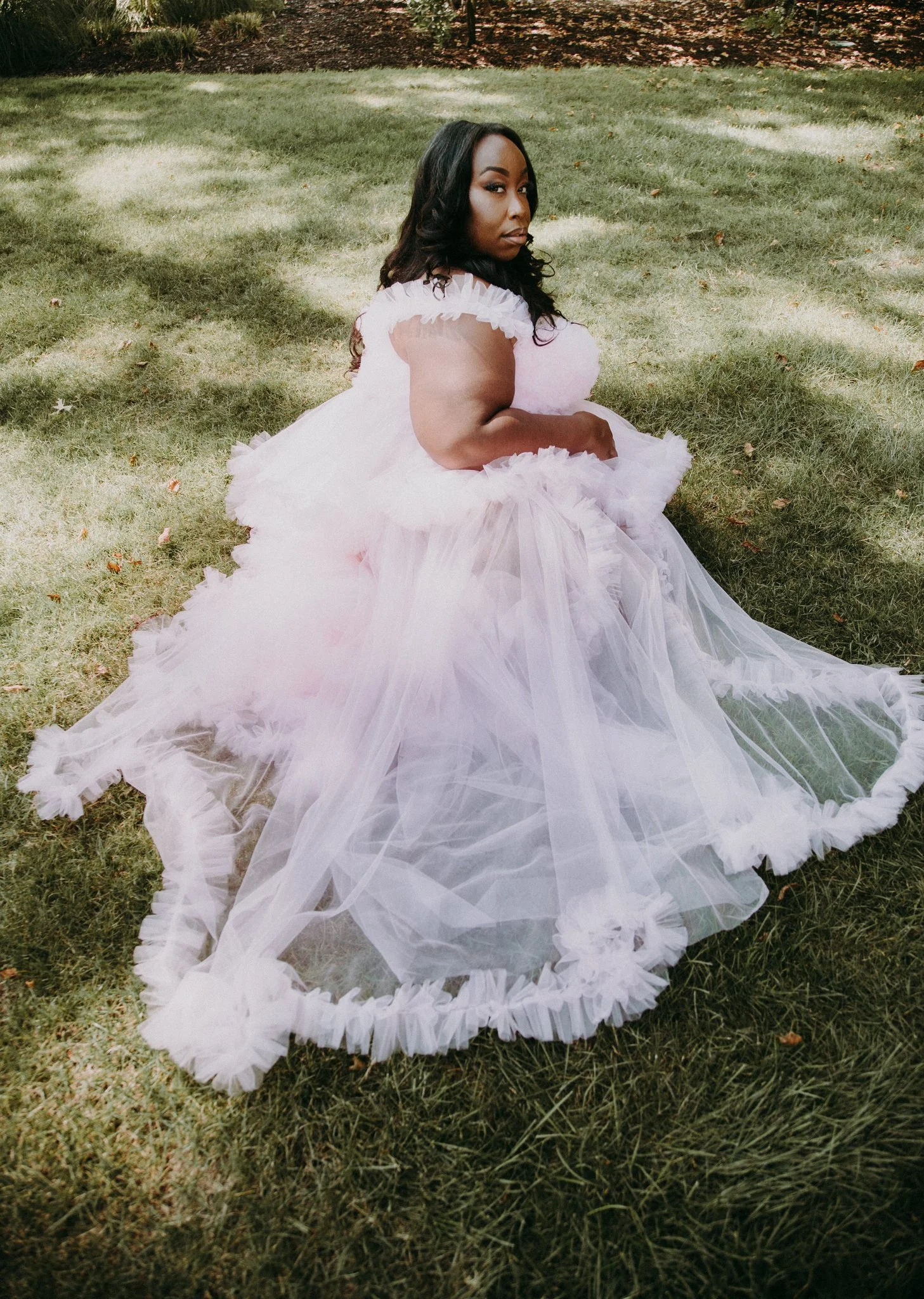 A pregnant person in a pink dress sitting in the grass 