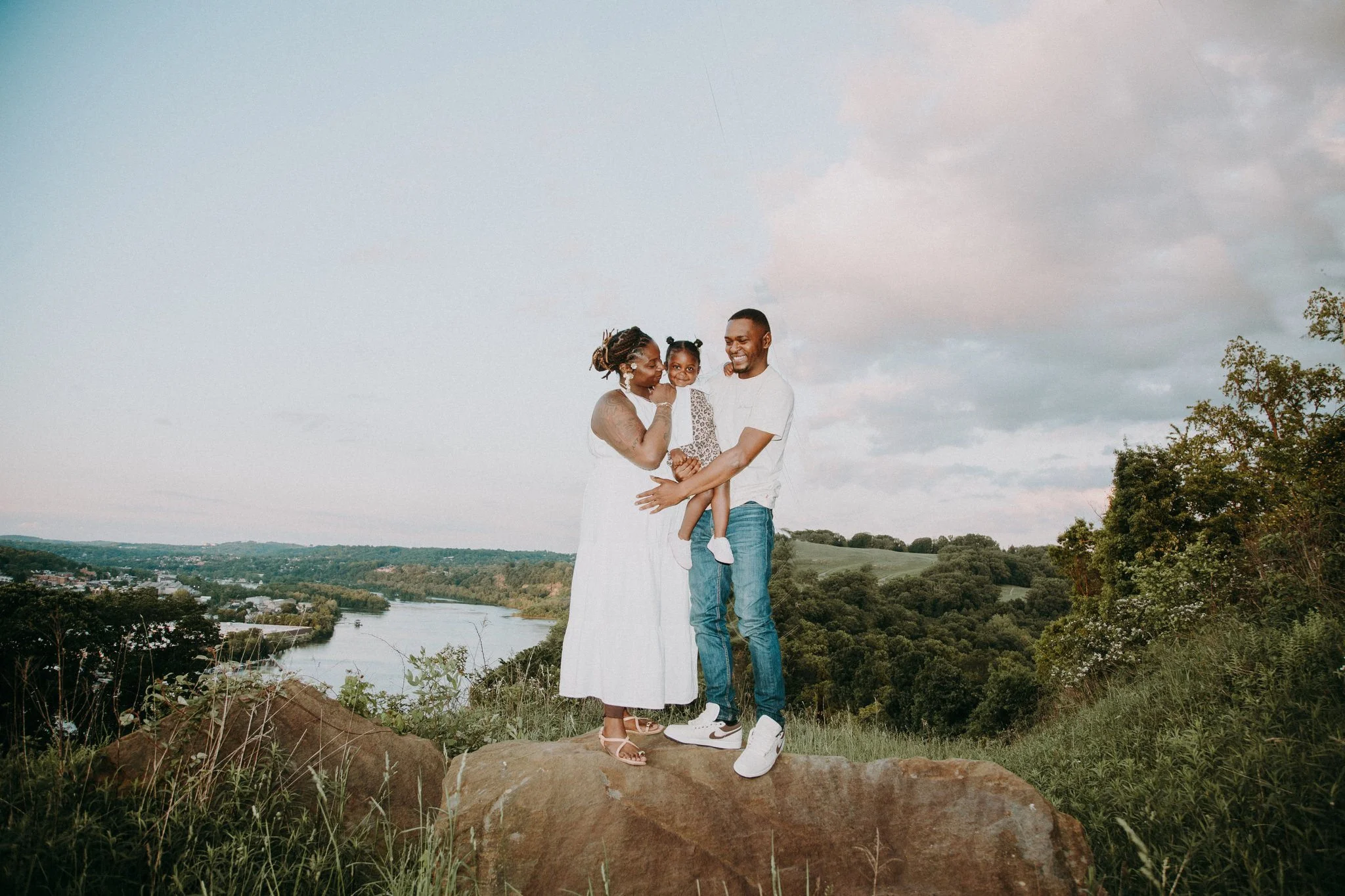 Two parents standing on a rock holding their child in between them 