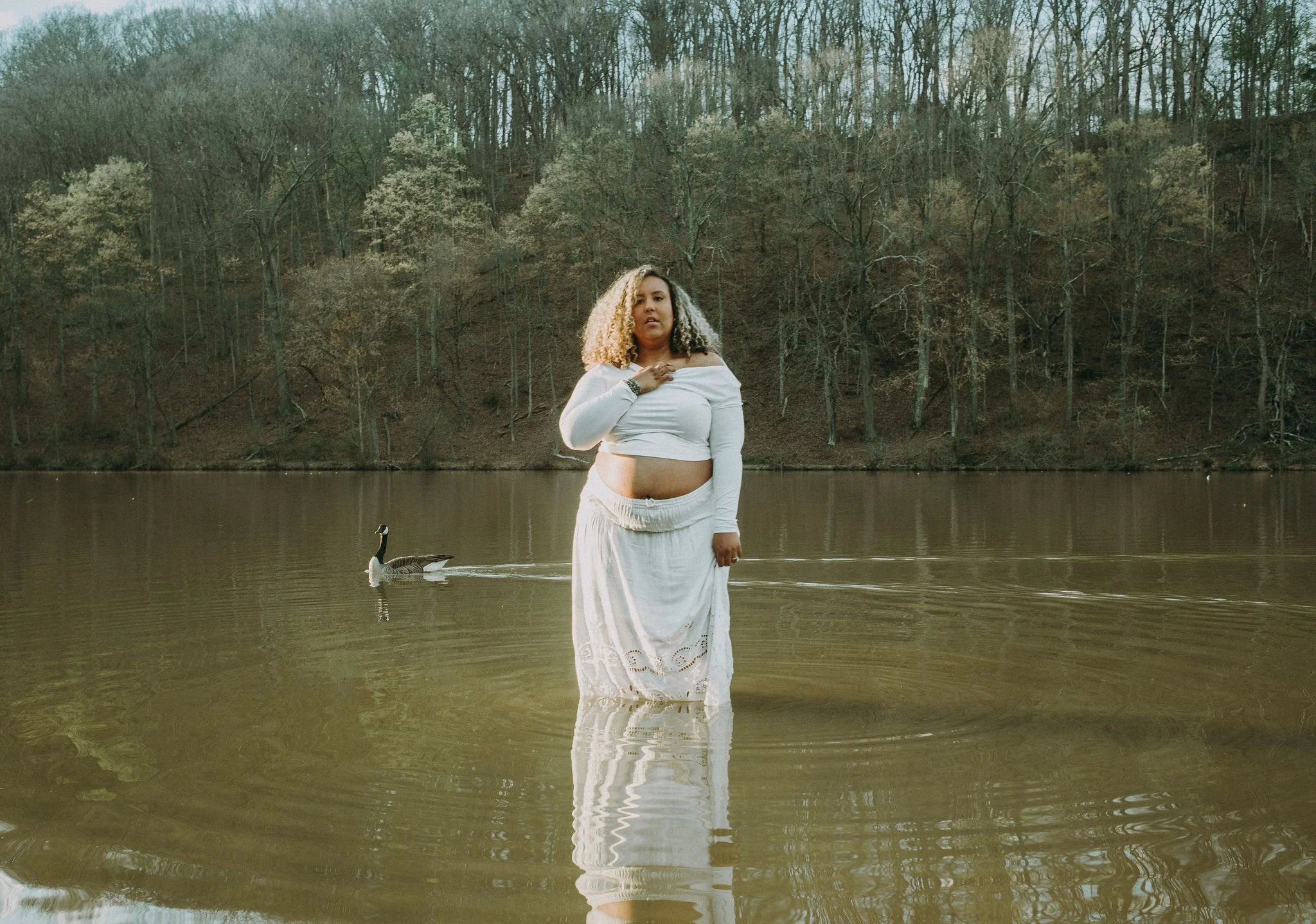 A pregnant person standing in shallow water 