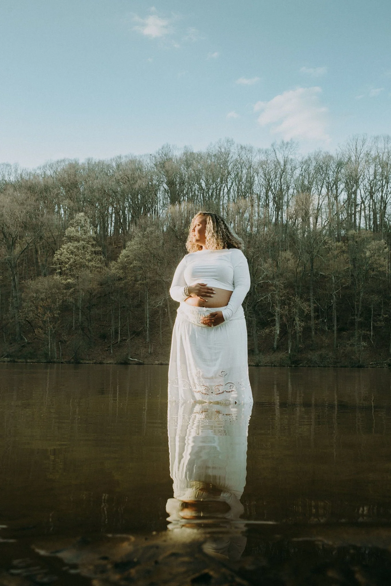 A pregnant person holding their stomach and walking through shallow water 