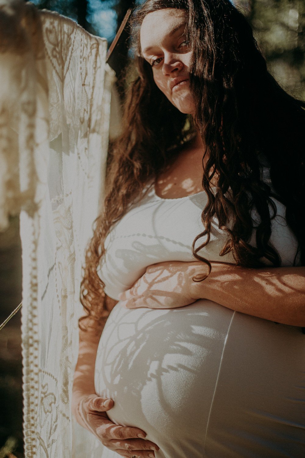 A pregnant person holding their stomach and standing next to a window 