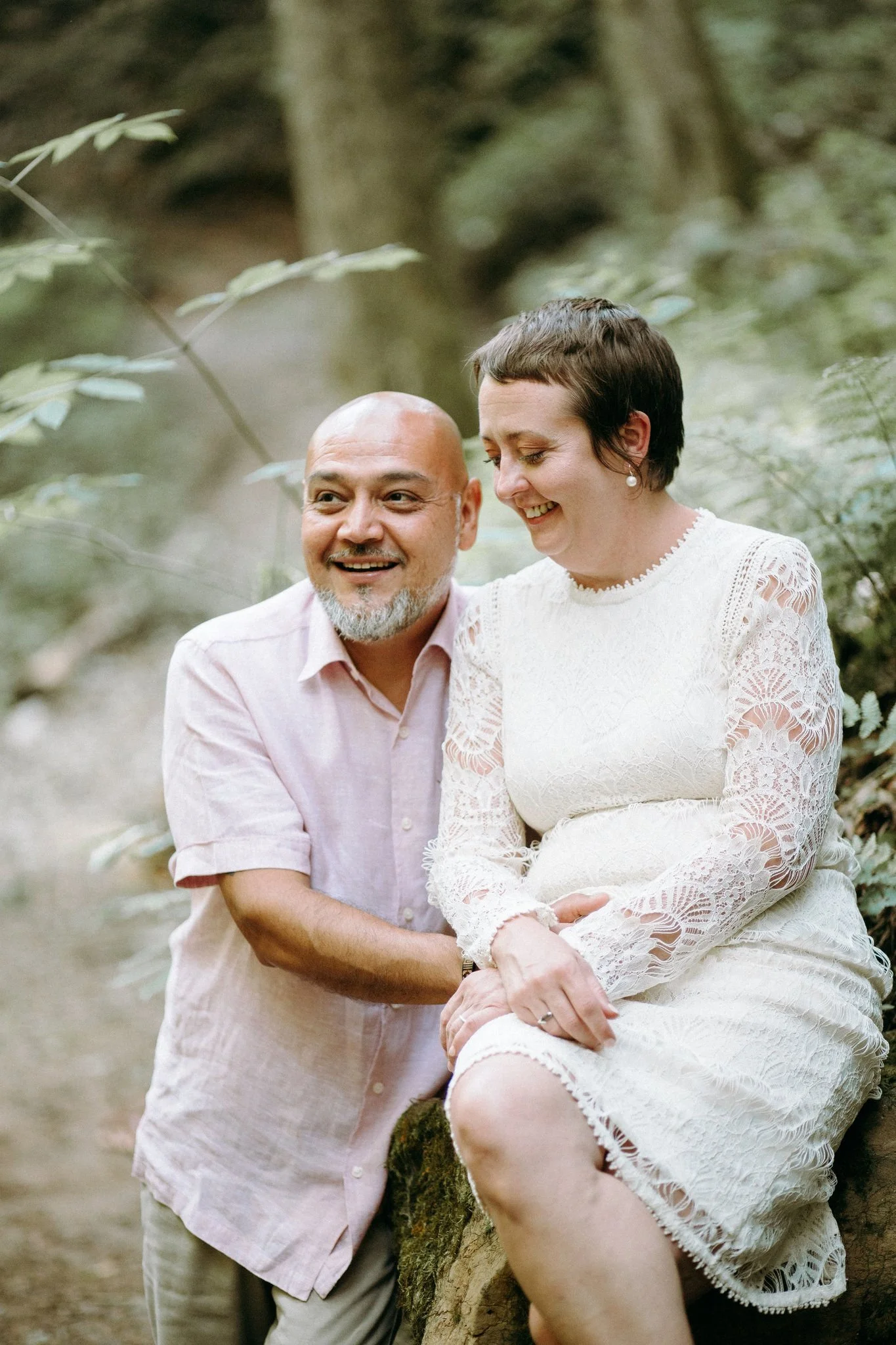 A person sitting on a rock smiling with their partner standing next to them