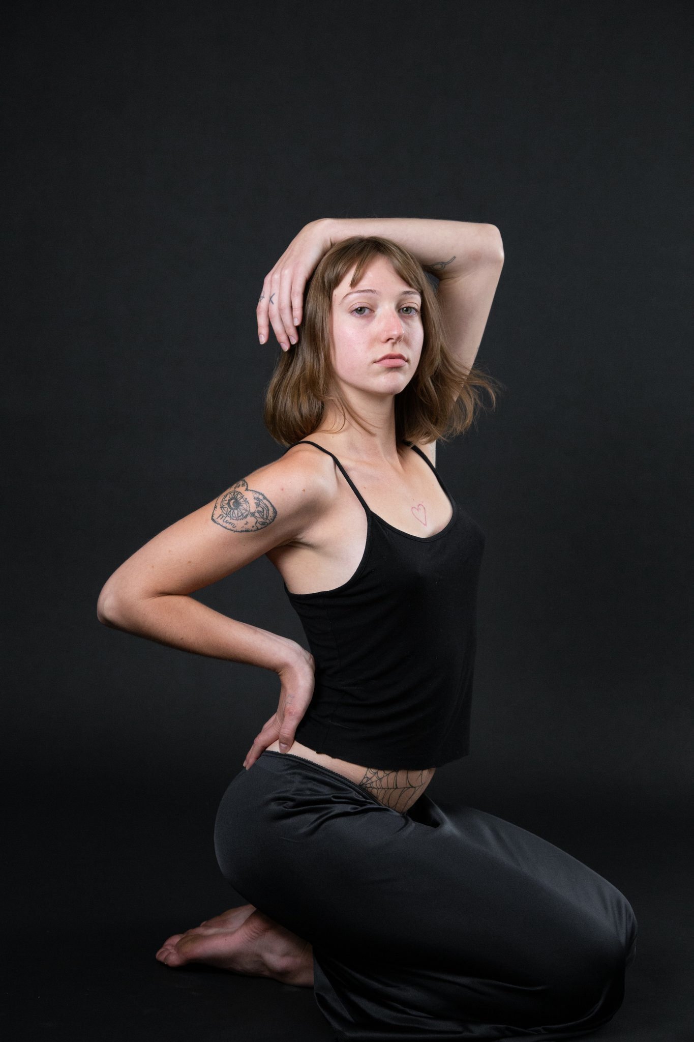 a person sitting on their knees with one arm over their head and the other on their hip