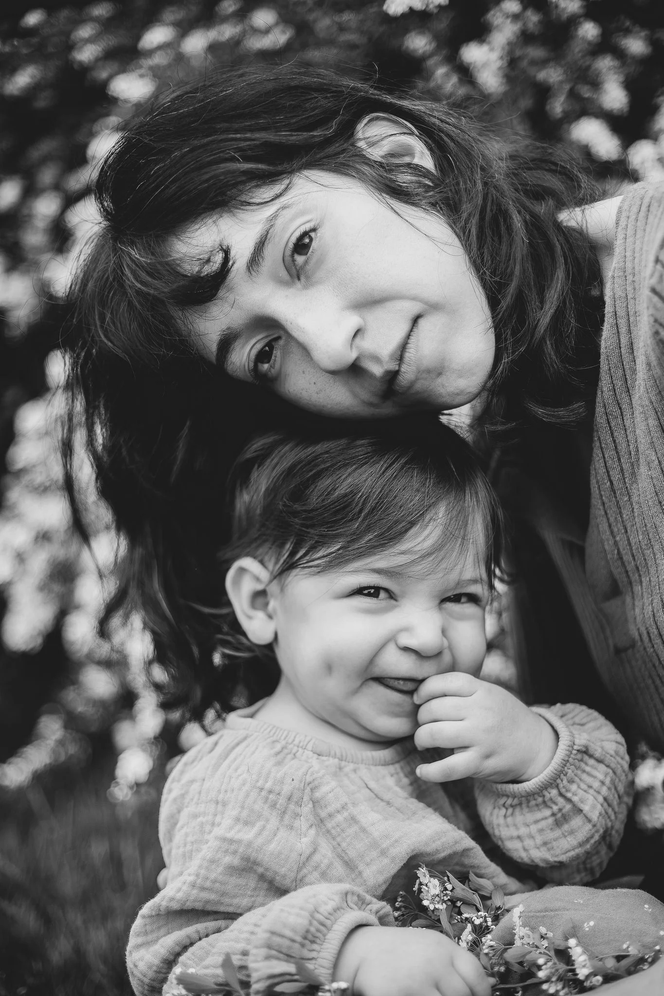A small child smiling as their parent lays their head on top of them