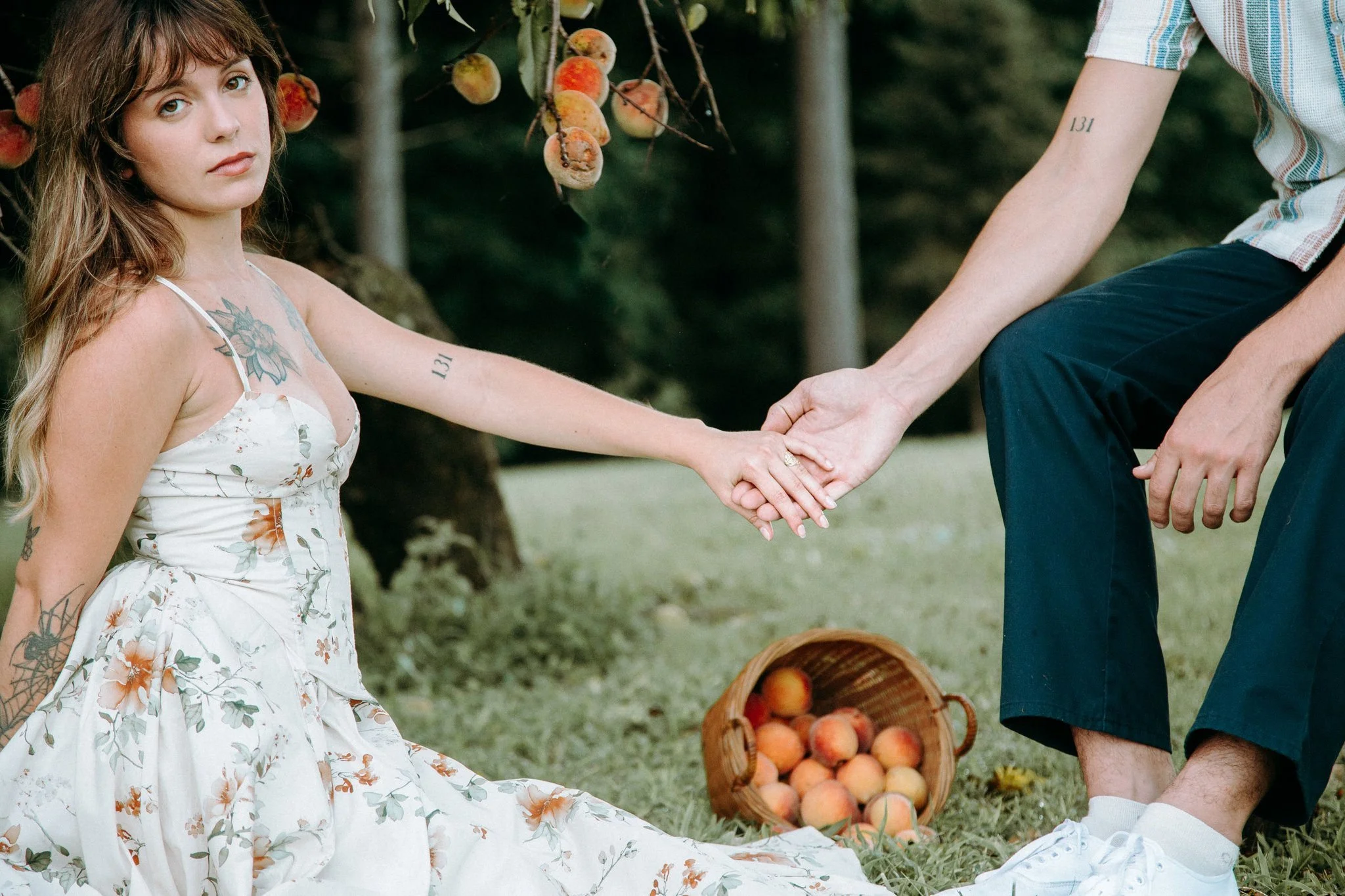 A couple sitting in the grass reaching out and holding hands 