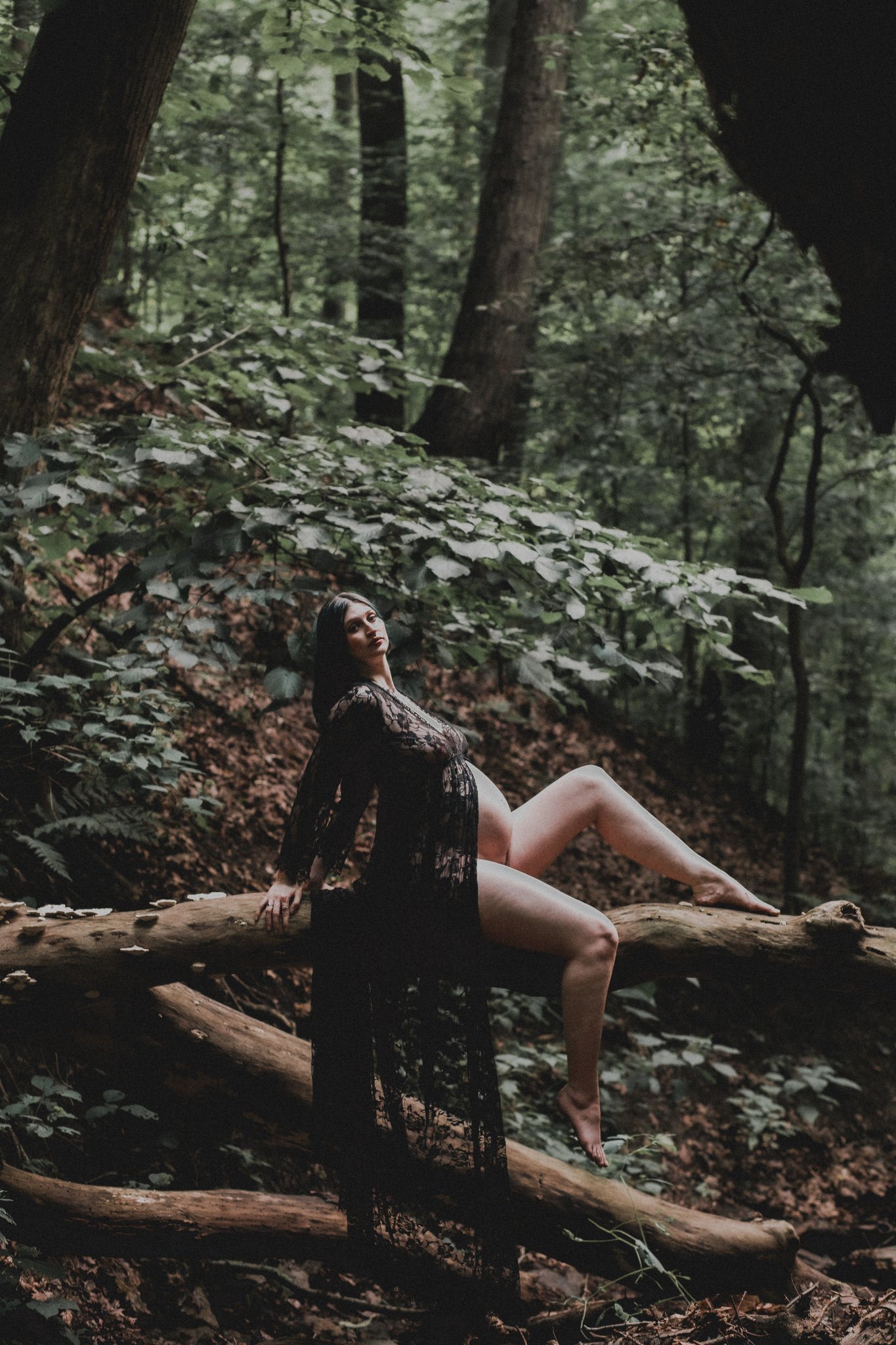 A pregnant person laid out on a log in the woods 