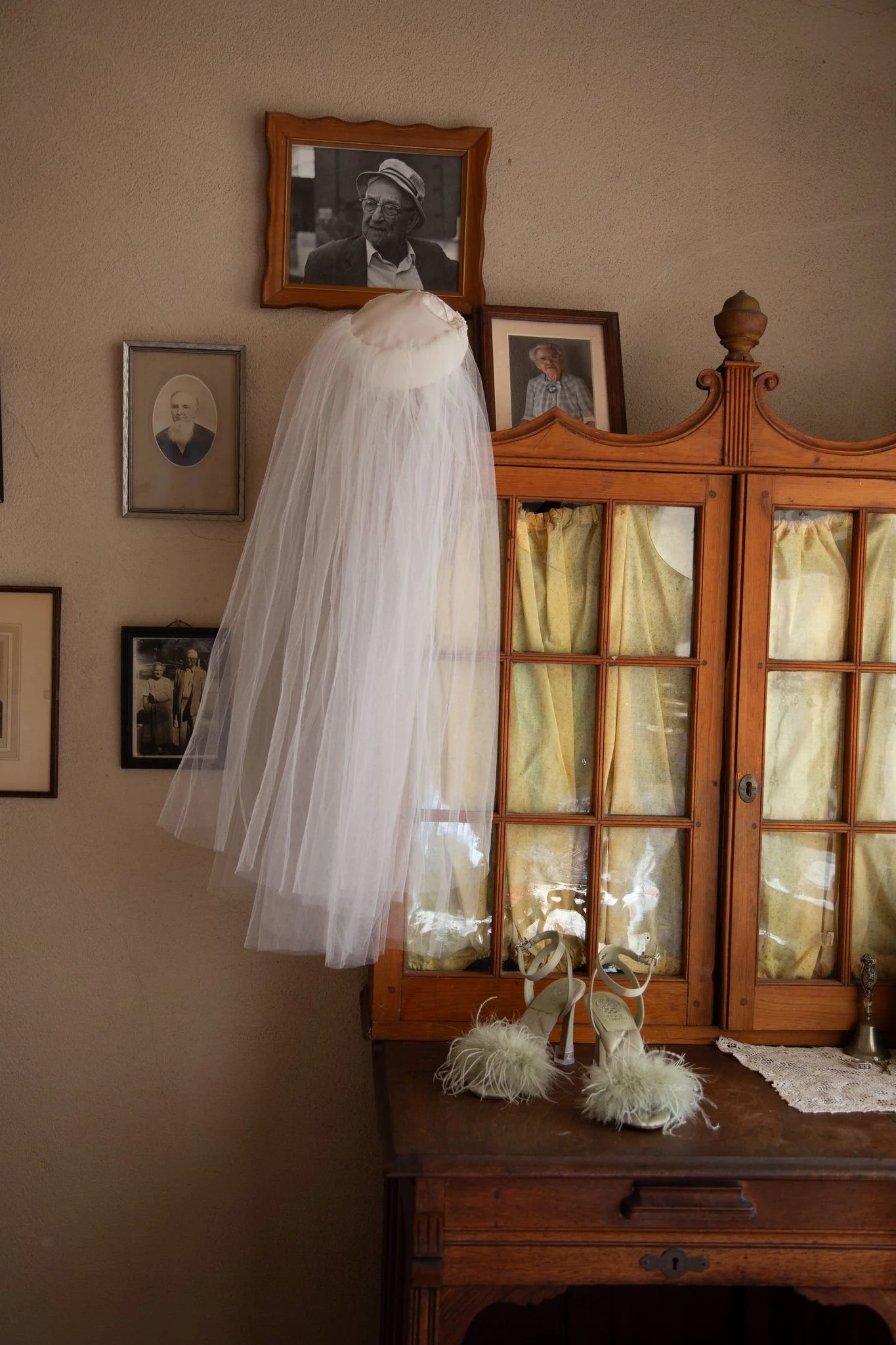 A veil hanging off the side of a wooden dresser with white heels sitting on top of it