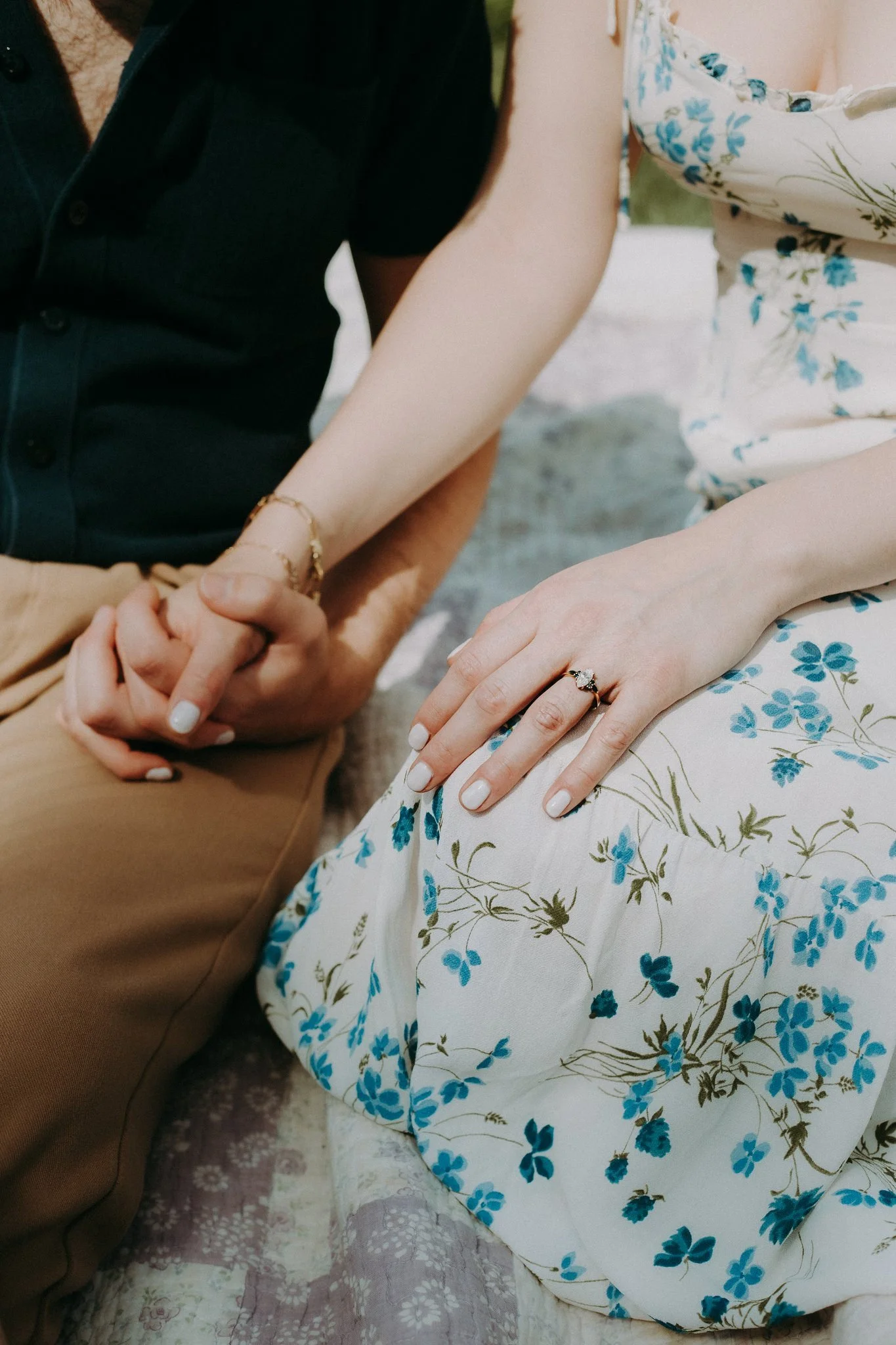 A close up of a couple holding hands and showing off an engagement ring 
