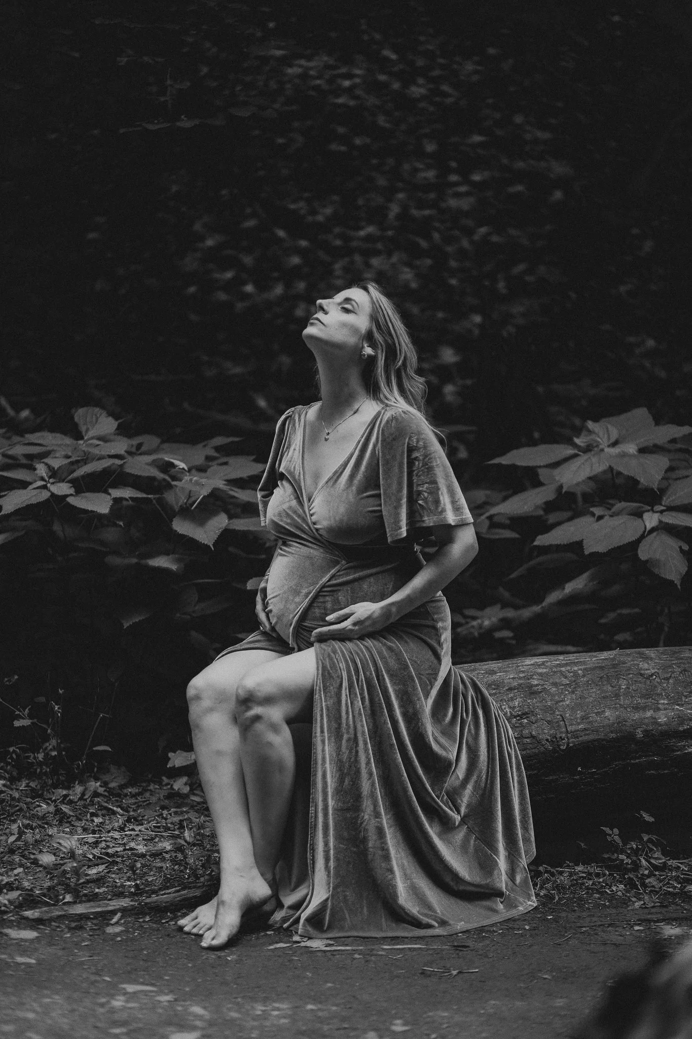 A pregnant person sitting on a log and looking up 
