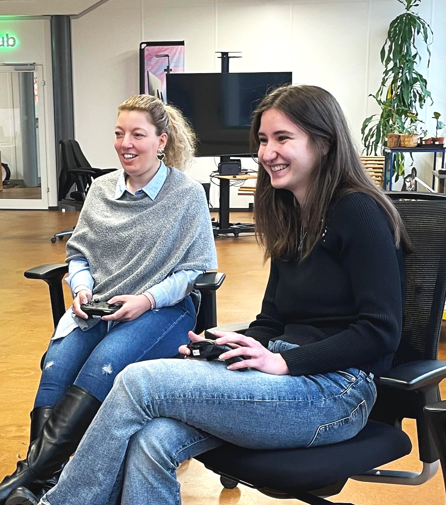 Zwei junge Frauen sitzen im Büro und spielen Videospiele, lachen und haben Spaß.