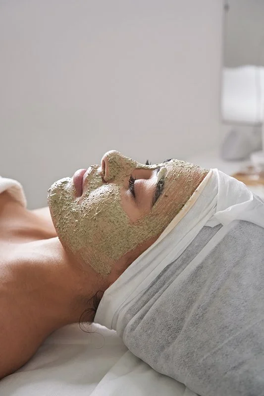 Persona recibiendo tratamiento facial con una mascarilla en un spa o clínica de belleza, acostada con la cabeza sobre una almohada.